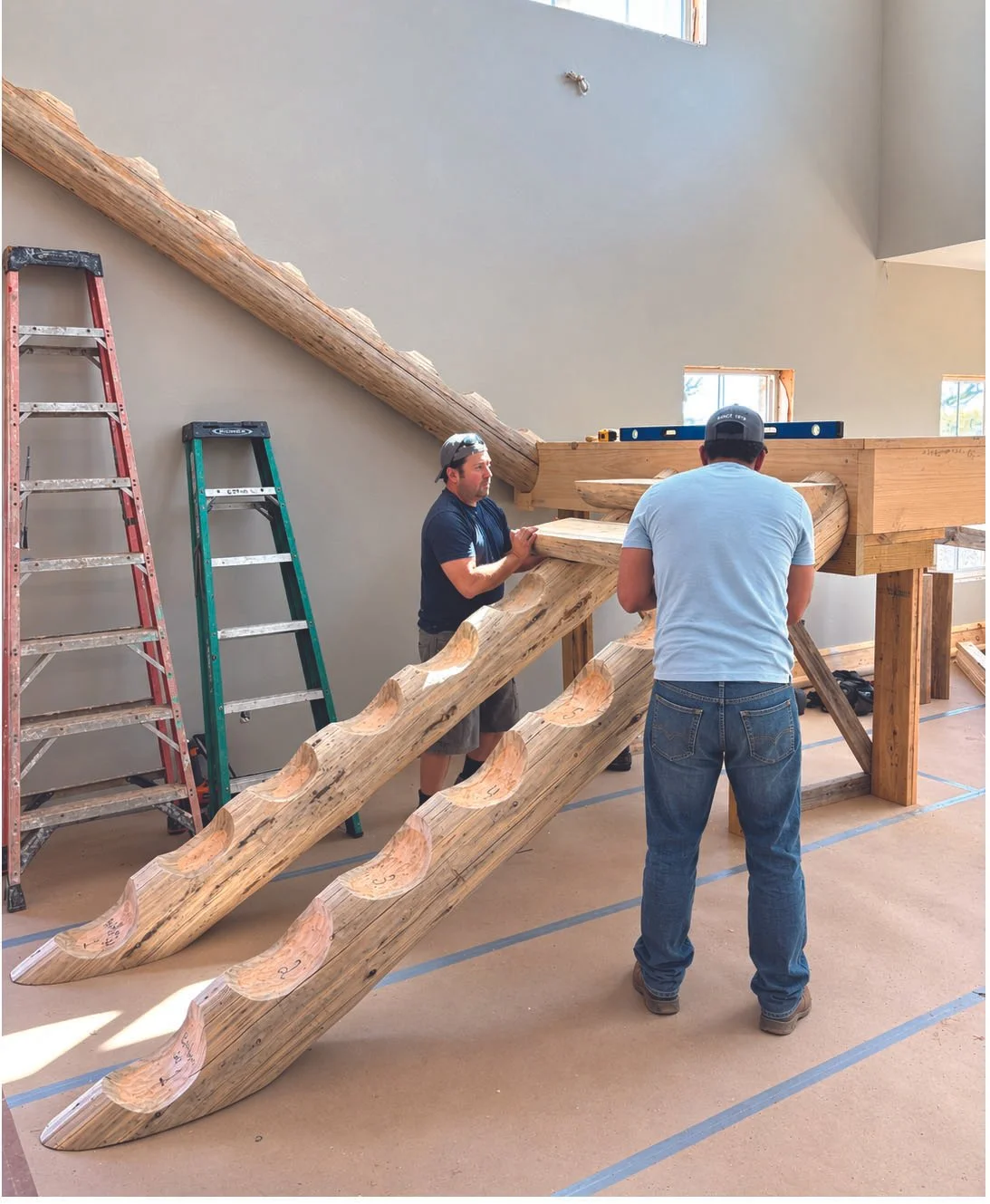Two men collaboratively constructing a large wooden staircase, focused on their task with tools in hand.
