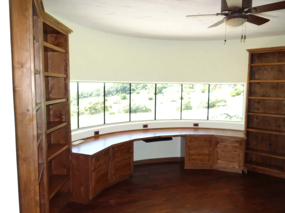 A corner desk positioned near a window, featuring a fan for ventilation and natural light.