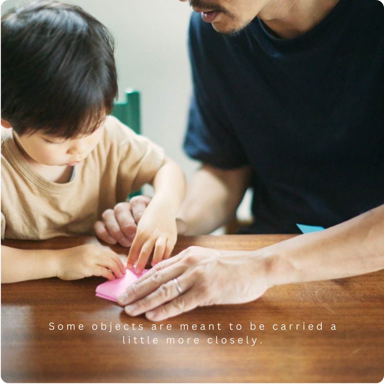 Father and young child folding origami together, reflecting shared ritual, care, and intergenerational connection.