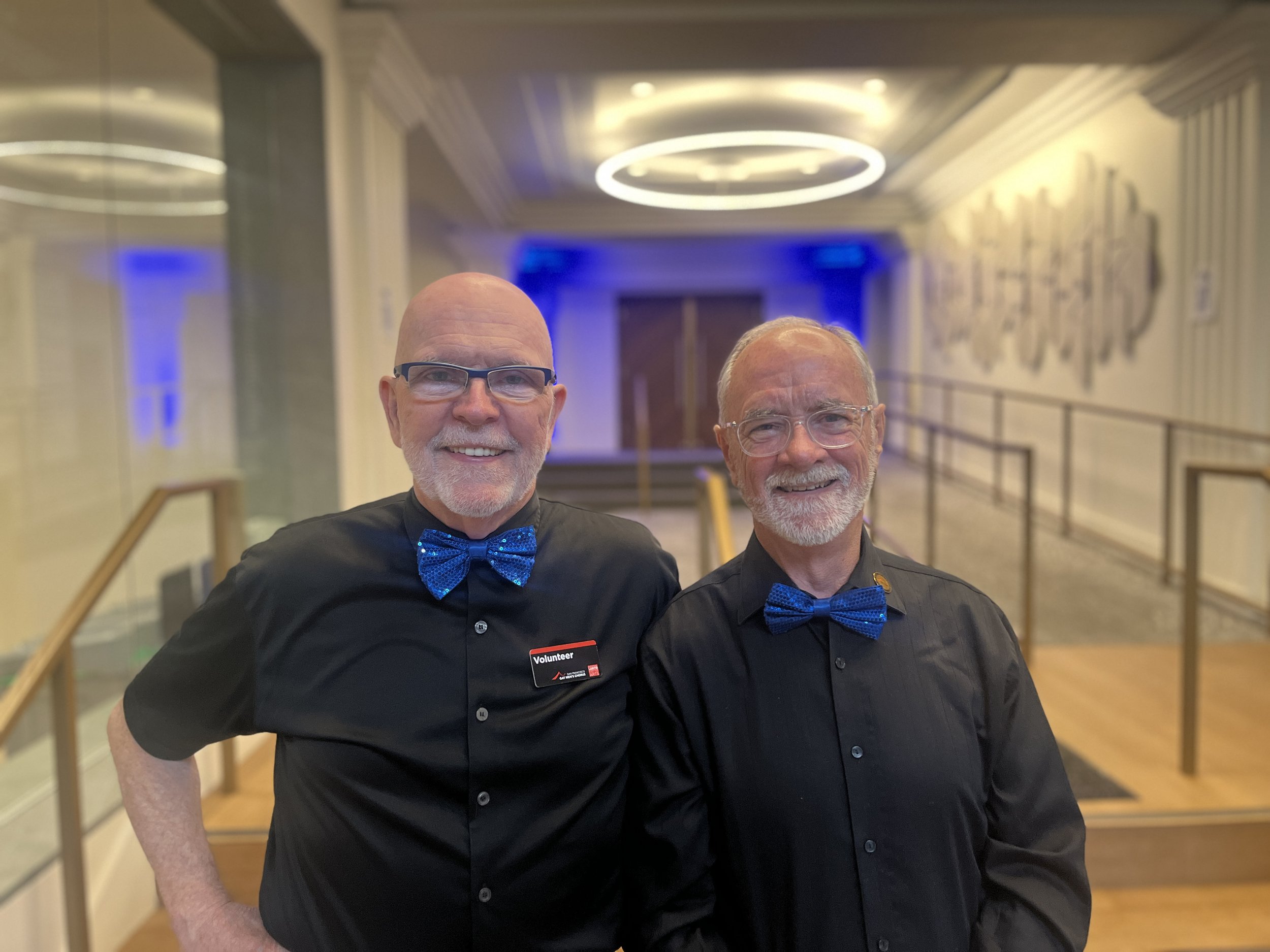 Two SFGMC volunteers wearing blue bow ties at The Chan National Queer Arts Center.