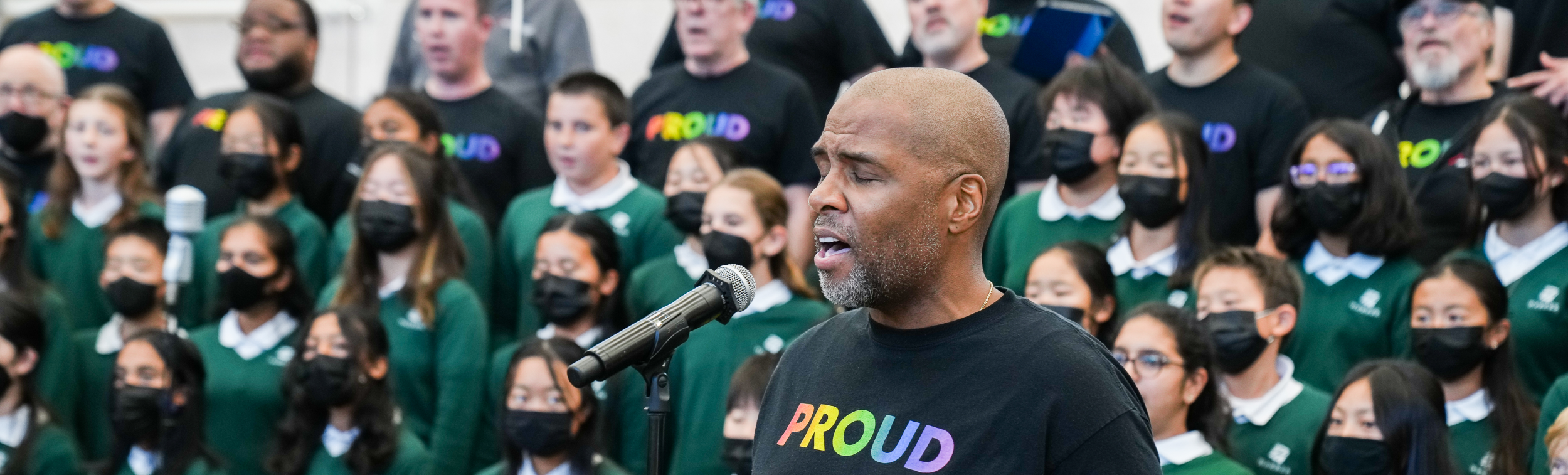 SFGMC singer performing during a RHYTHM school assembly with students and Chorus members behind him.