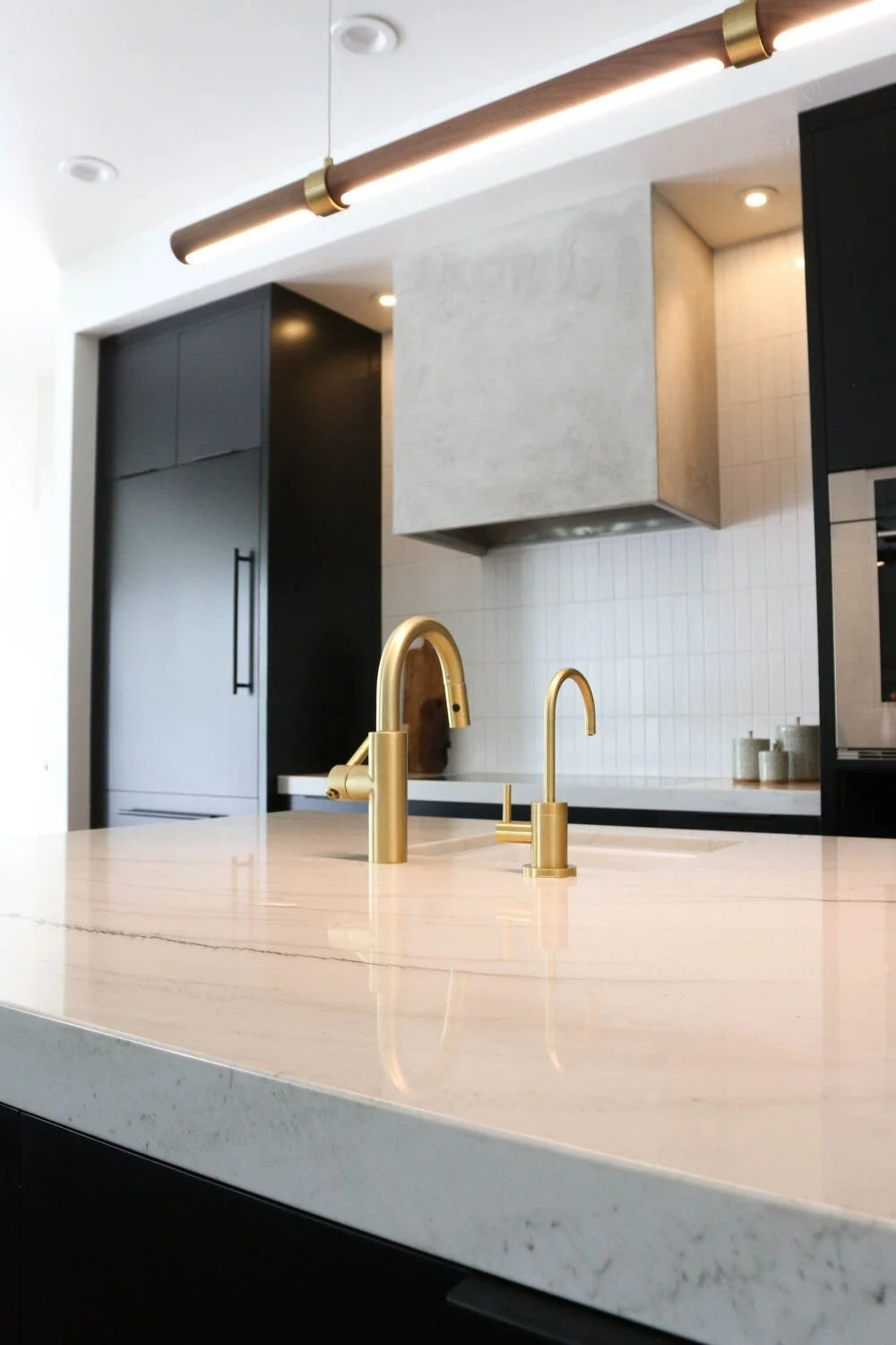 Modern kitchen with marble countertop, gold faucets, black cabinets, tile backsplash, and sleek lighting.