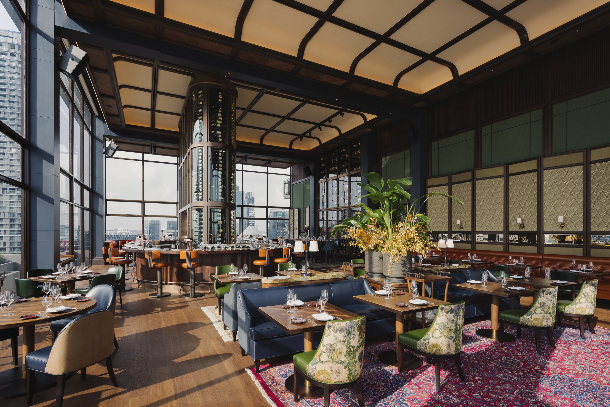 Elegant dining room at 67 Pall Mall Singapore featuring a central glass wine display, modern furnishings, floor-to-ceiling windows and city views. Photographed by Daniel Koh.