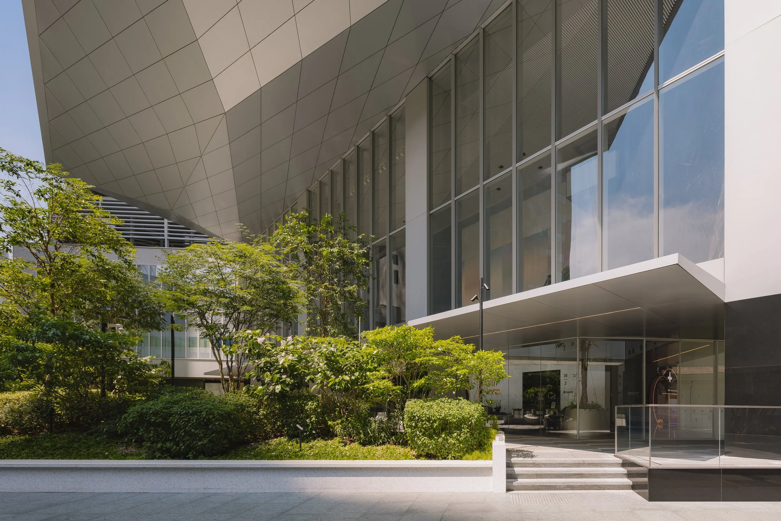 Singapore Land Tower in Singapore, featuring the landscaped entrance plaza by Henning Larsen, lush planting, dramatic cantilevered canopy and contemporary glass façade. Architectural photography by Daniel Koh.