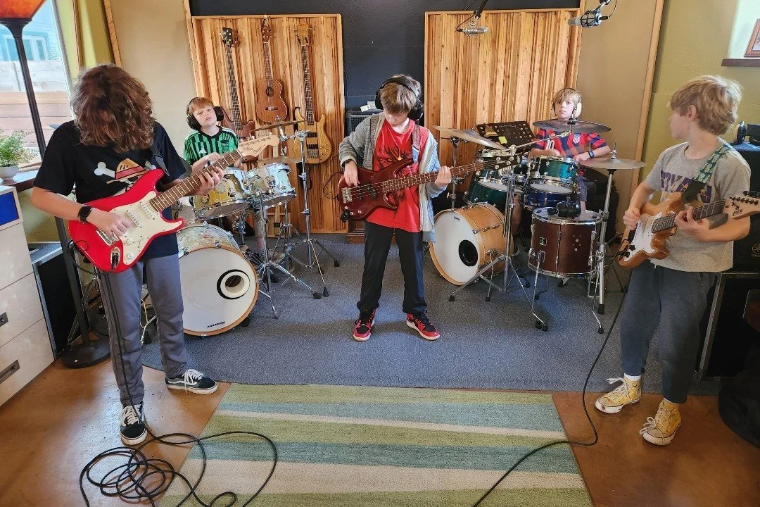 Five We Love Music students playing guitar, bass and drums together in a band rehearsal
