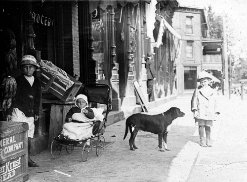 Children wait patiently with their dog “Spot” on the sidewalk outside Hobart Edwards’s Grocery Store at 105 West Liberty Street while their “Mom” shops for the family daily supply of food in 1912