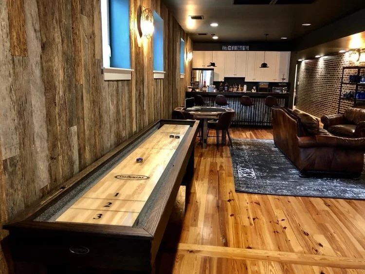 Indoor game room with air hockey table, seating area with brown leather couches, and a bar in the background.