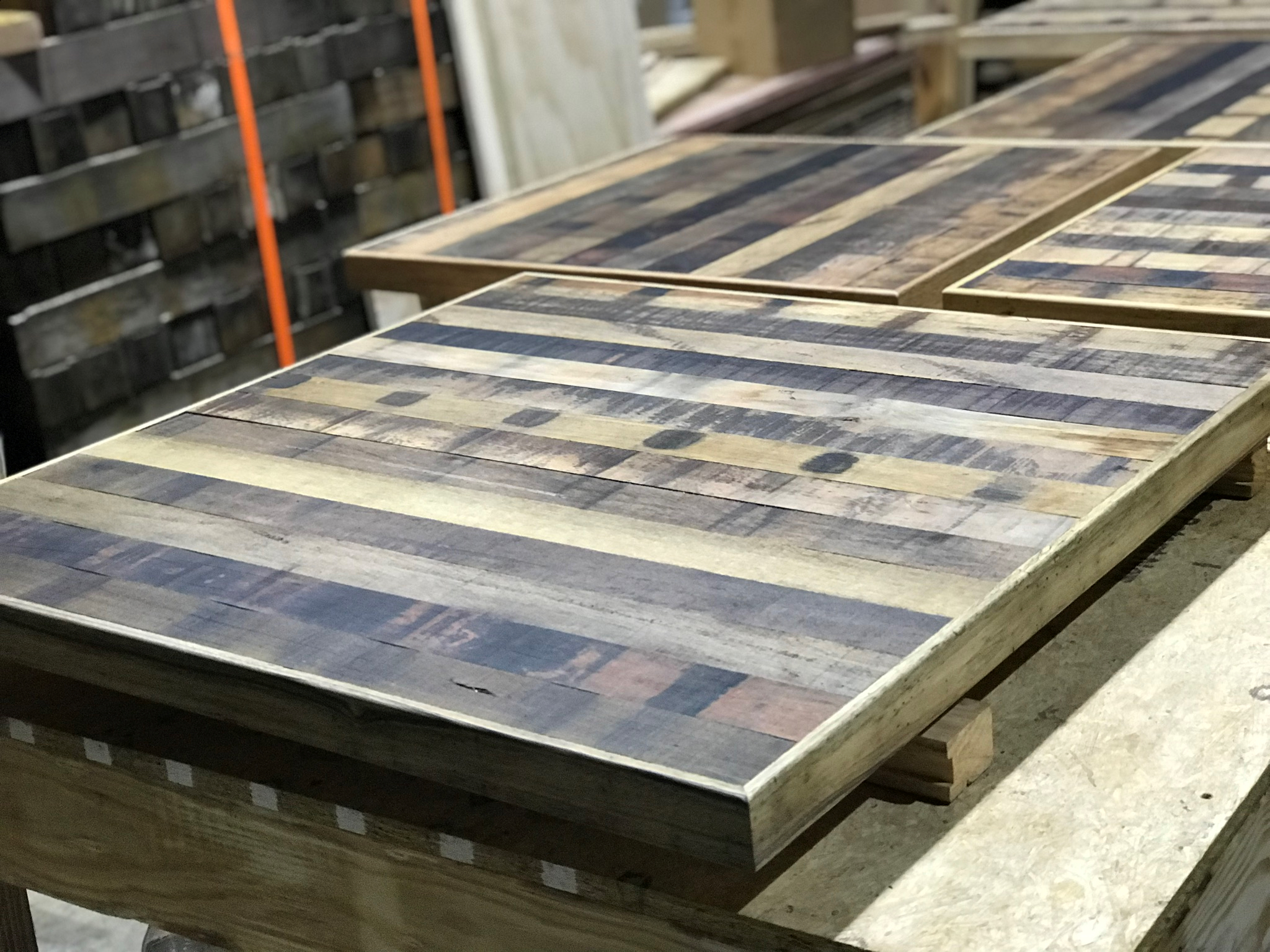 Wooden pallets with recycled wooden boards arranged for a project in a workshop. The boards have mixed wood patterns and are placed on a wooden work surface.