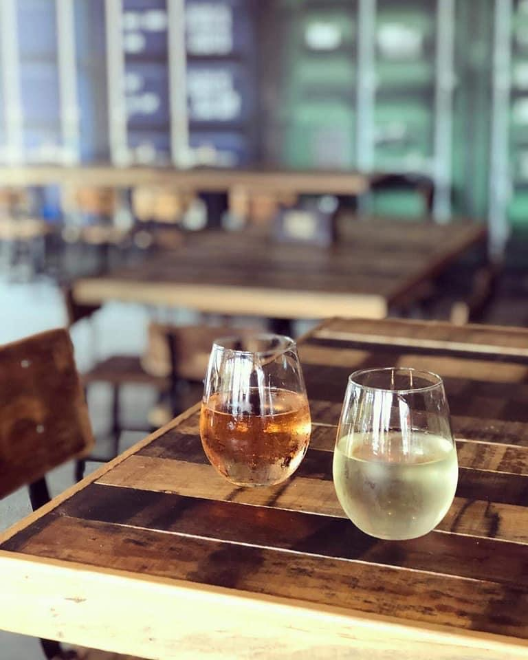 Two glasses of white and rosé wine on a wooden table in a rustic restaurant or cafe setting.