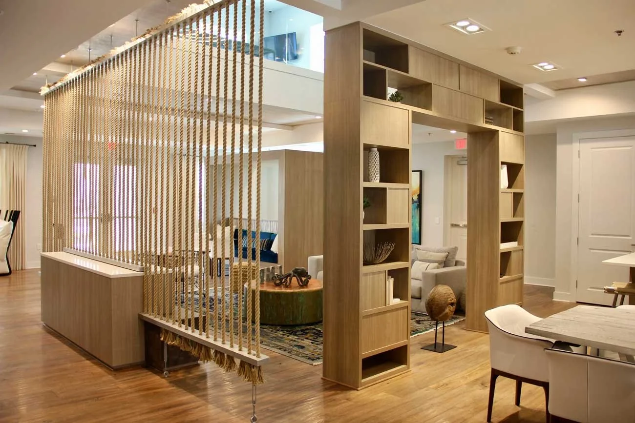 Interior view of a modern apartment or hotel living space with wooden shelving, a lattice divider, and furniture including a dining table and chairs.
