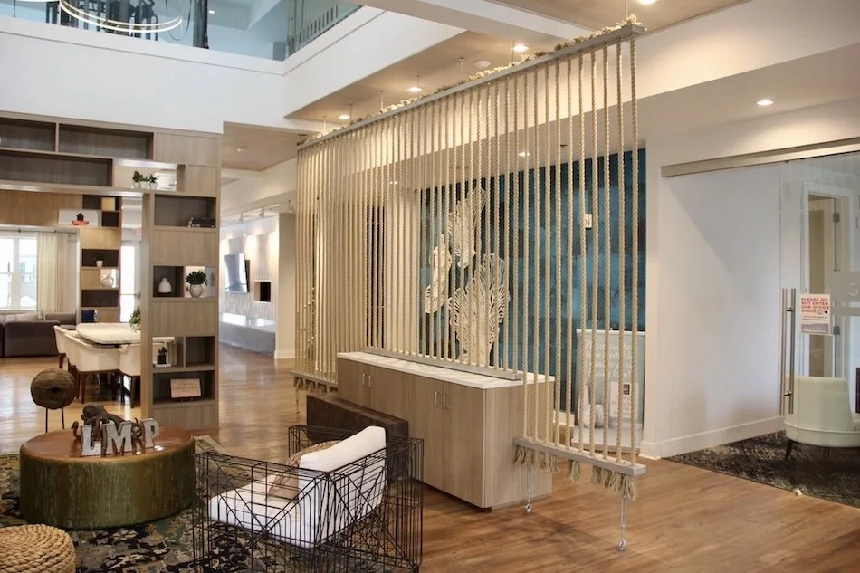 Modern interior of a building with decorative wooden slats in front of a staircase, a round table, seating area, and bookshelf.