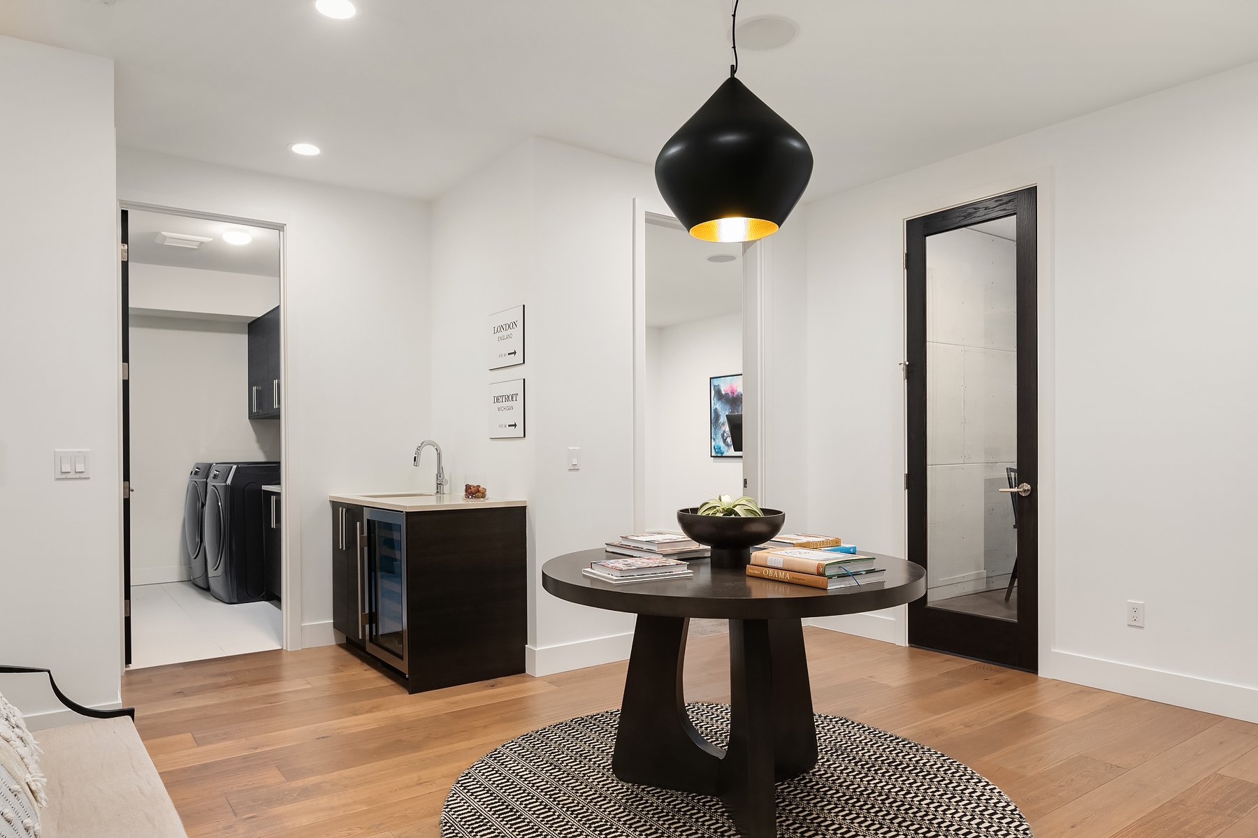 When you head downstairs, you reach this open foyer-room for a large table and bench plus a sink and wine fridge. In the background you can see the laundry room, the door in the middle is up for grabs, but currently used as a workout room. The door 