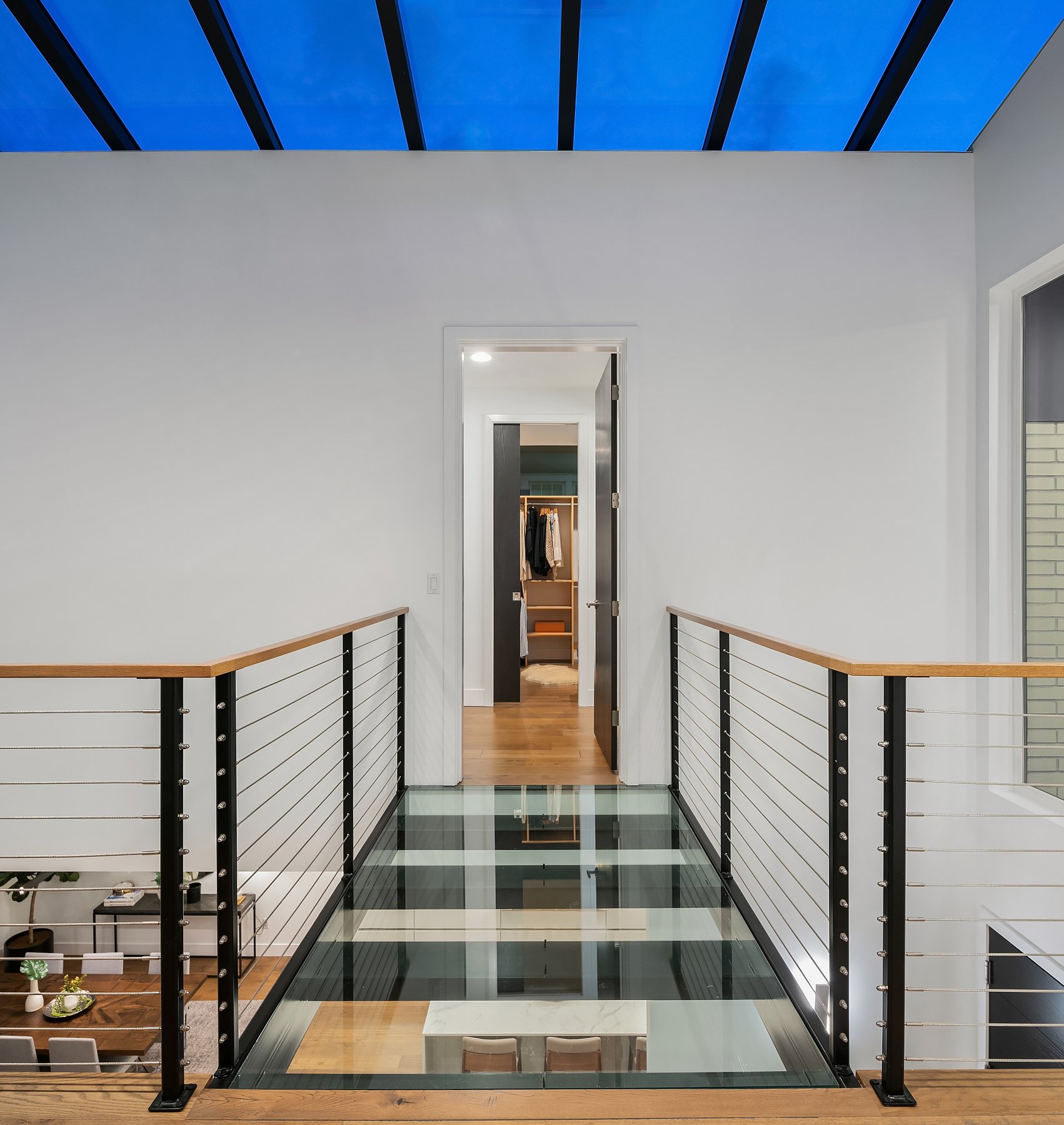  Up to the second floor… Modern stainless railings line the hall and a glass-floored bridge connects the primary bedroom to the rest of the second floor. Notice the skylights above that provide the drams and also flood the home with happy sunshine du