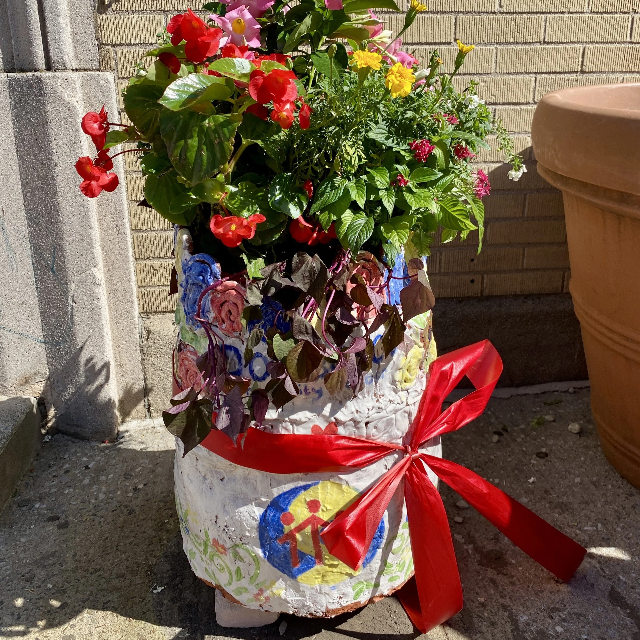The painted planter stands in front of Don Bosco, full of colorful flowers.