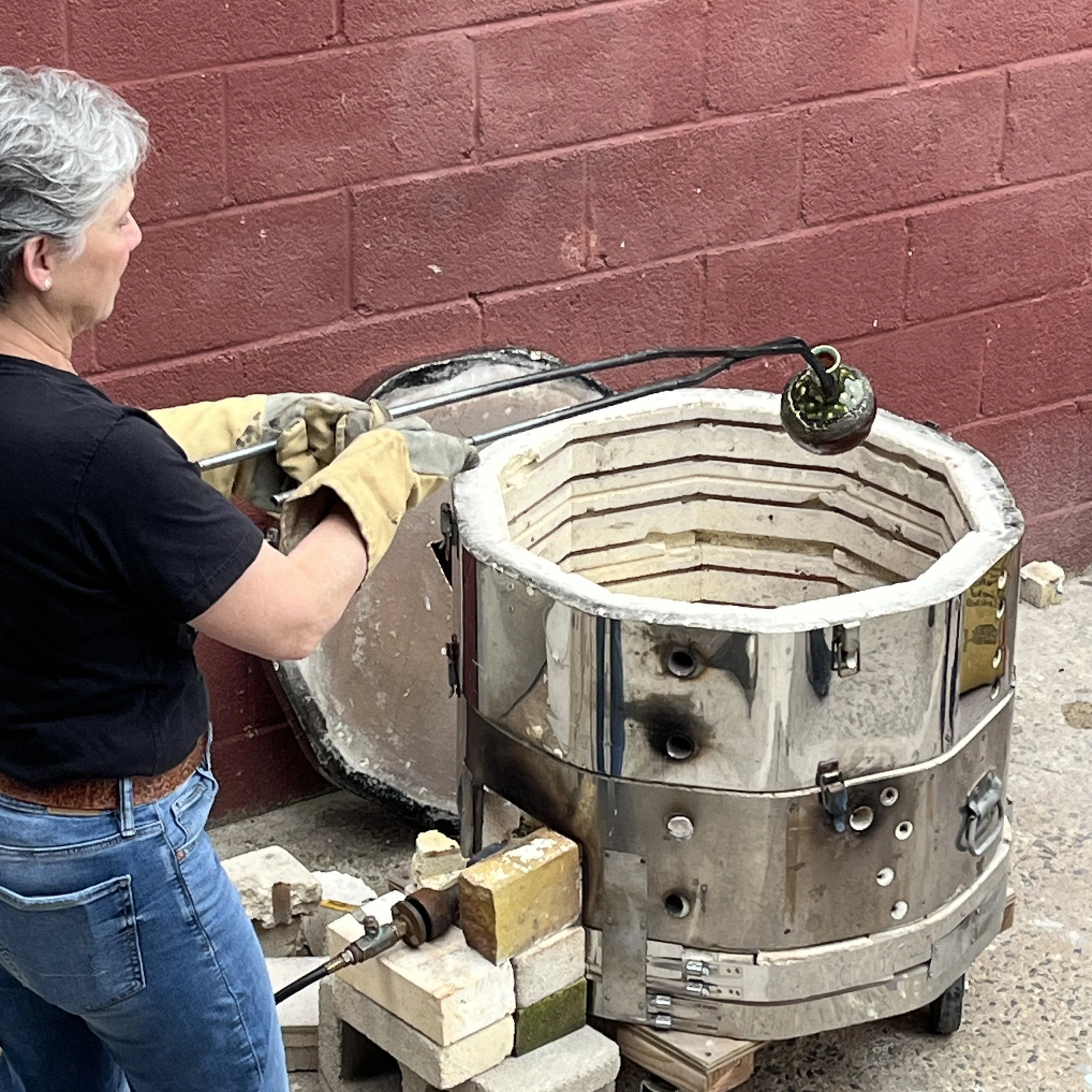 Wendy lifts a pot from the raku kiln.