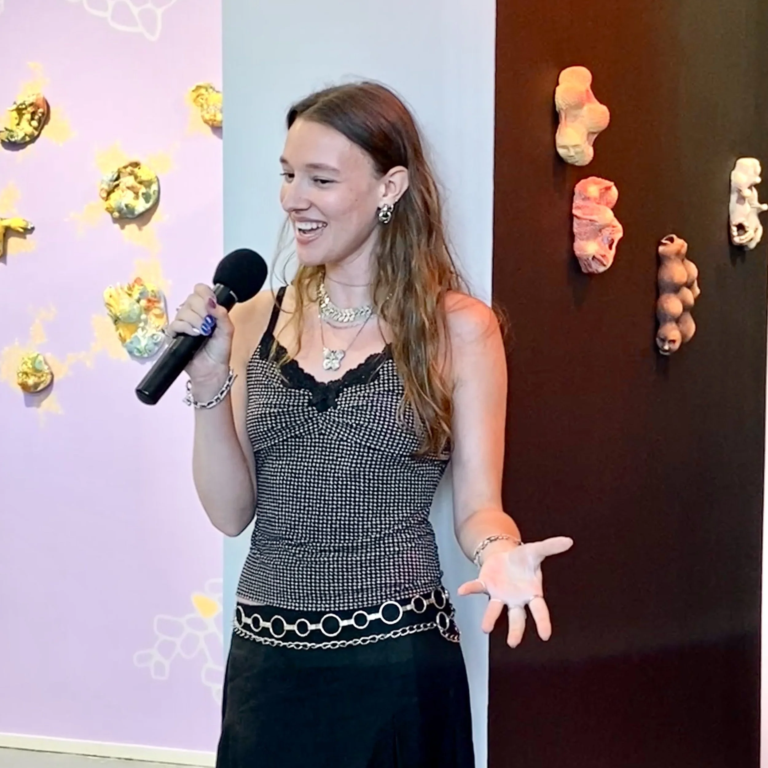 Carley stands in front of the Artist-in-Residence exhibitions speaking into a mic