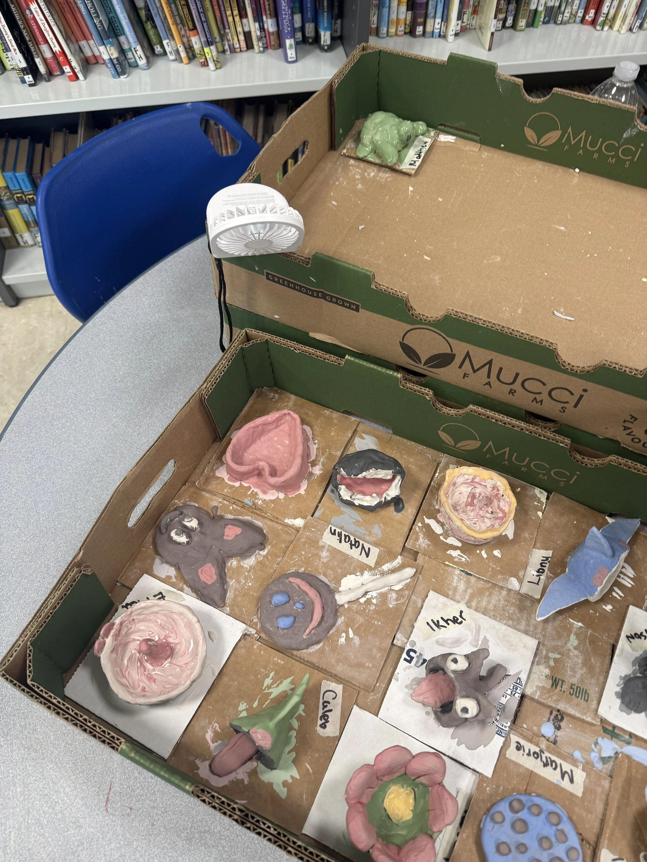 A box of colorful pinch pot projects, including a heart, a smiley face, and various creatures