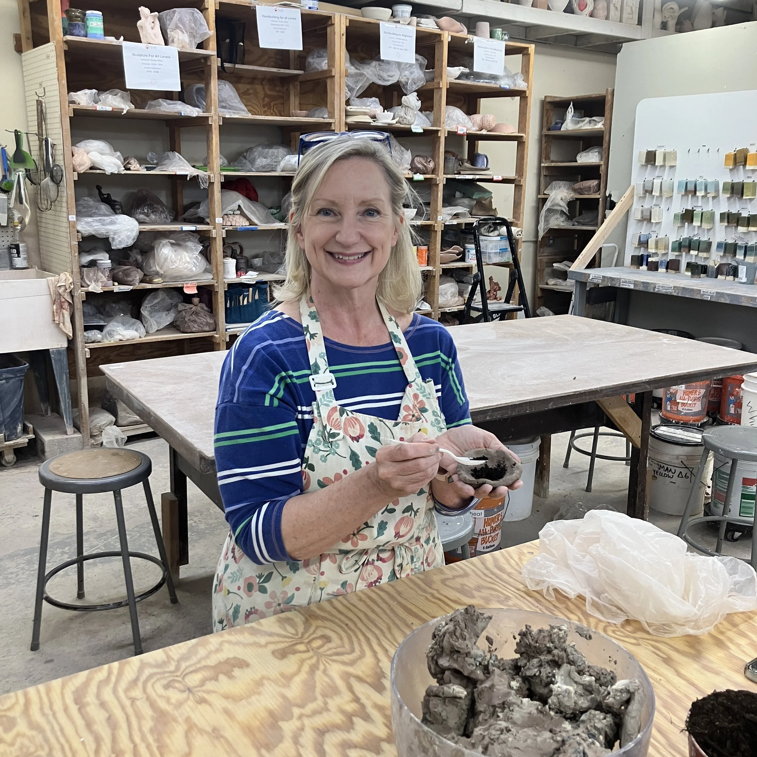 Jen uses a spoon to add seeds to the soil-filled piece of clay in her other hand