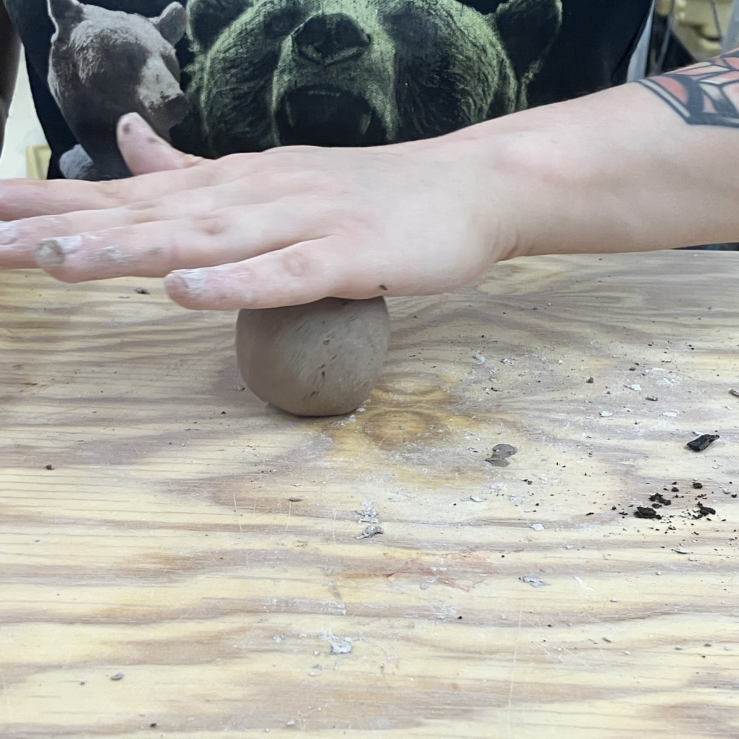 A hand rolls the spherical seed bomb on a wooden table