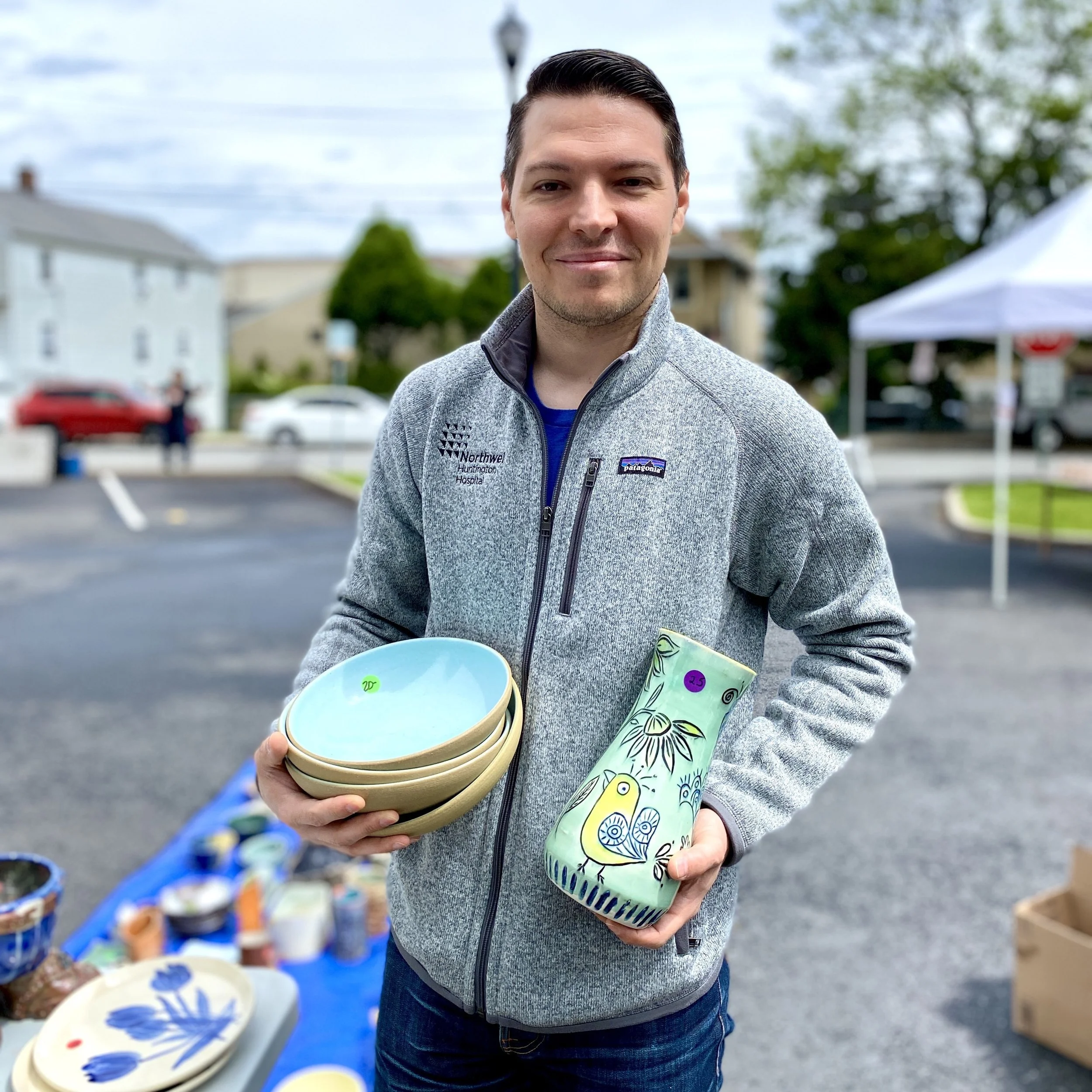 A man holds his finds from the potter sale: a stack of pasta bowls and a blue vase with a bird on it