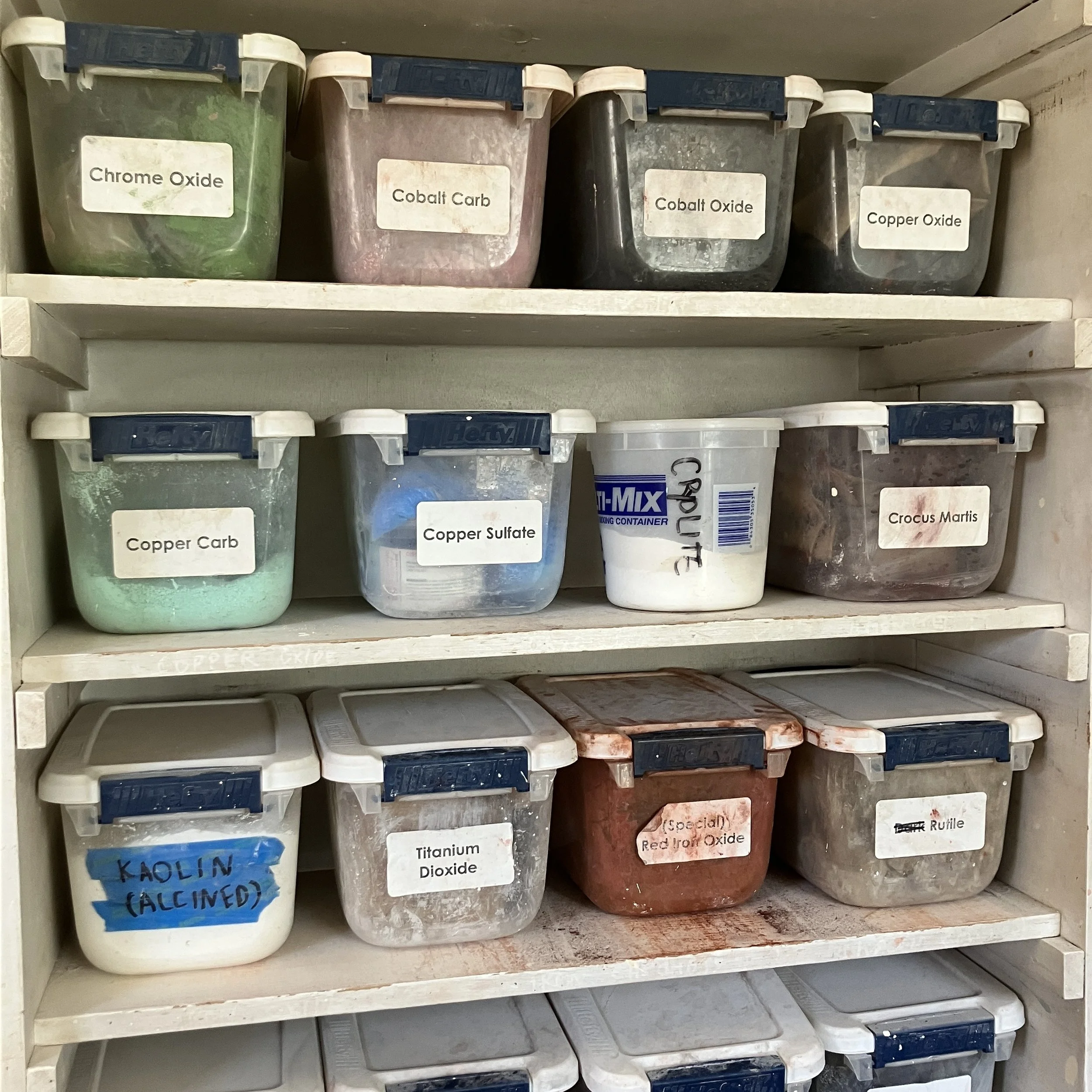 A book shelf of individual glaze components in small plastic bins. The bins are labeled with the names of the contents.