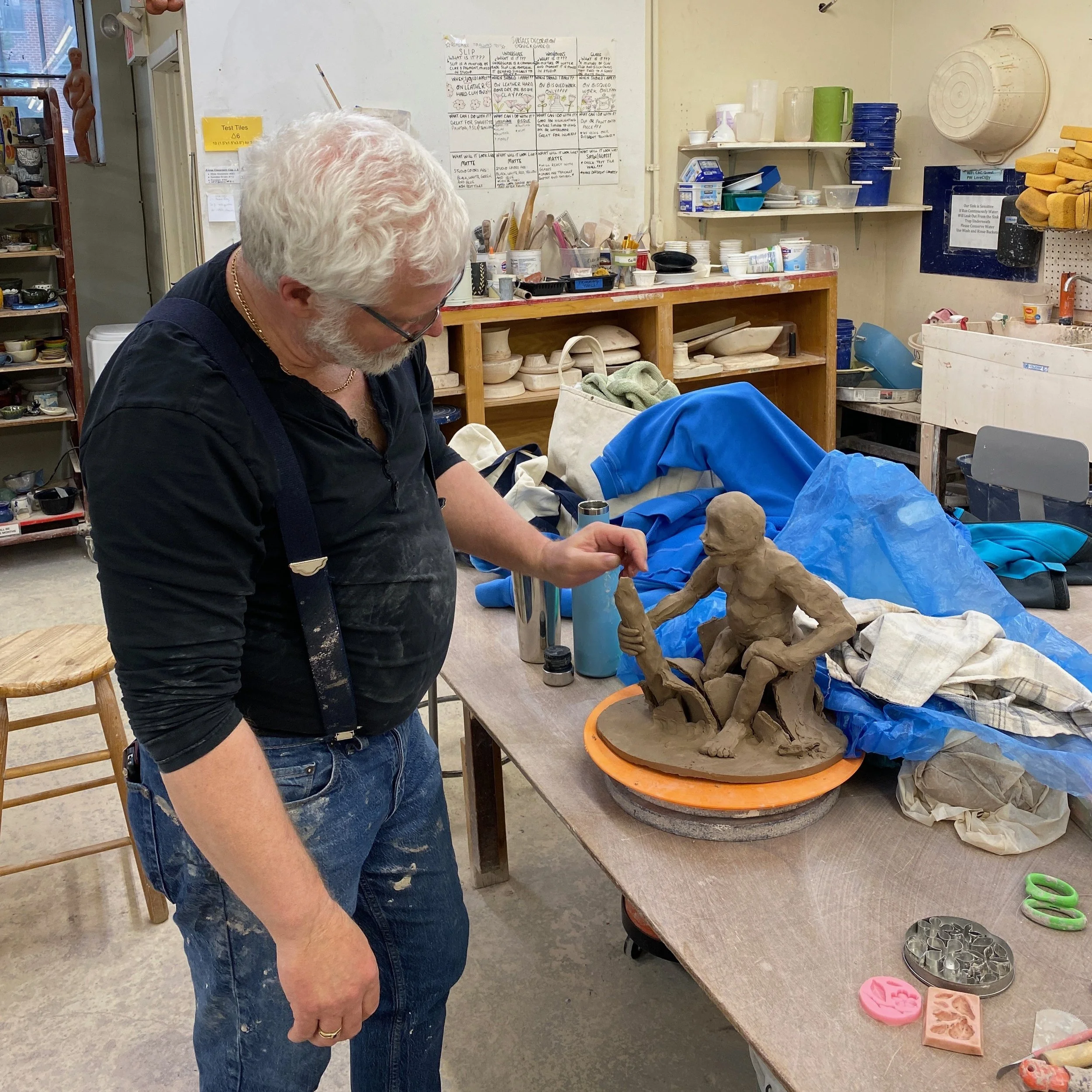 Jeff reaches out to touch his sculpture of a seated humanoid figure, still in its raw clay form.