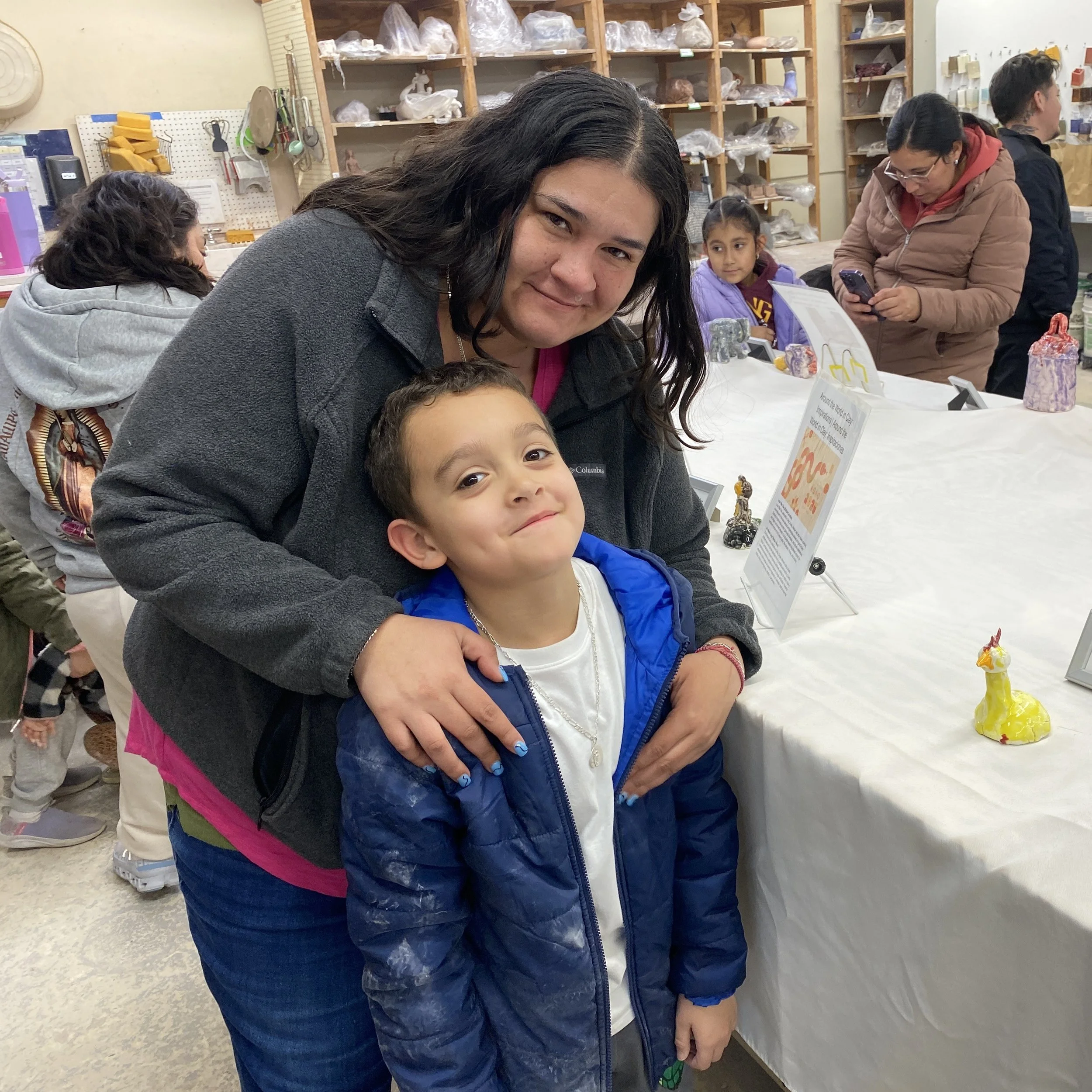 A mom holds her son, who made ceramic work in the show, from behind.