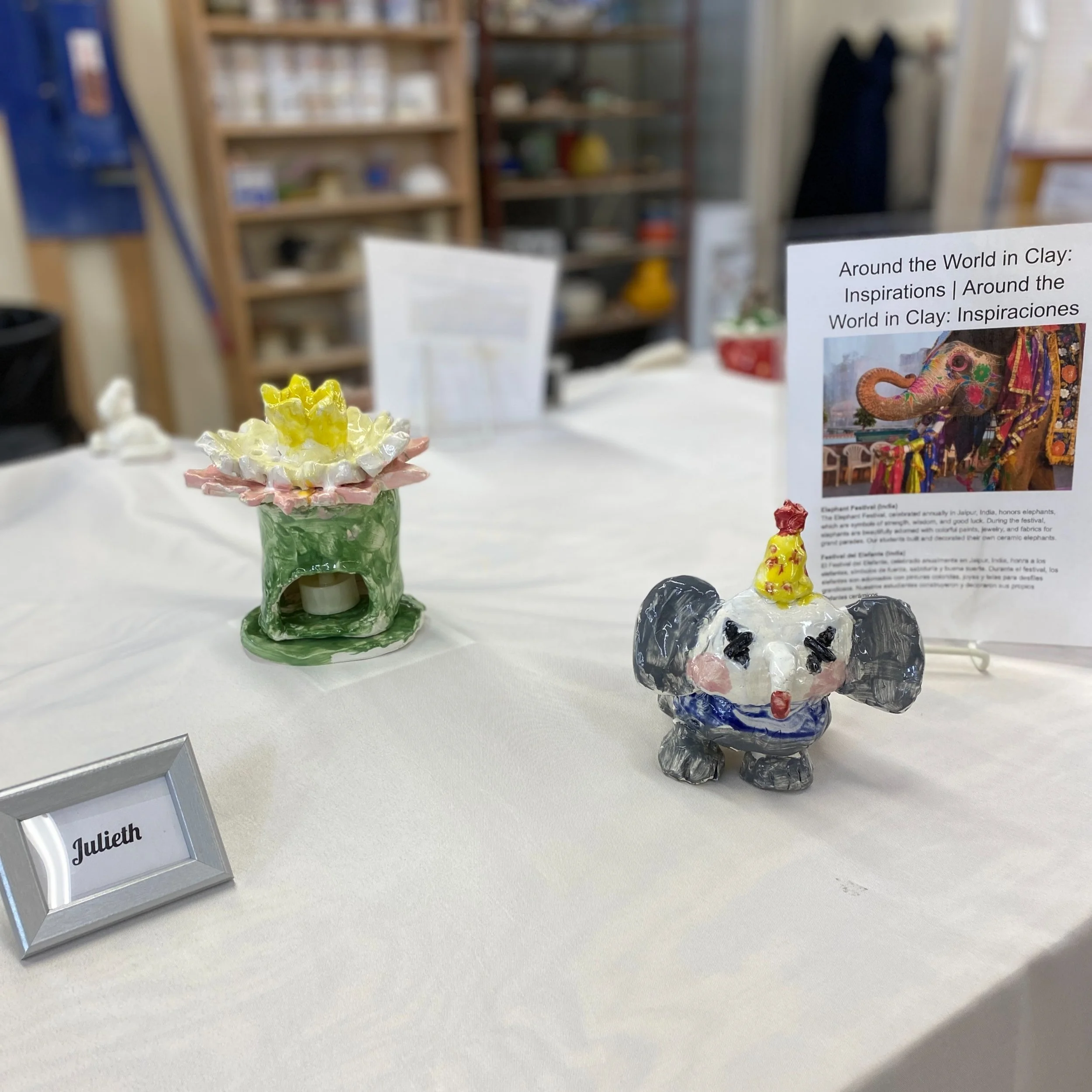 A sculpture of a clown elephant and a colorful ceramic luminary with an LED tealight inside sit on the table next to a nametag that reads, "Julieth."