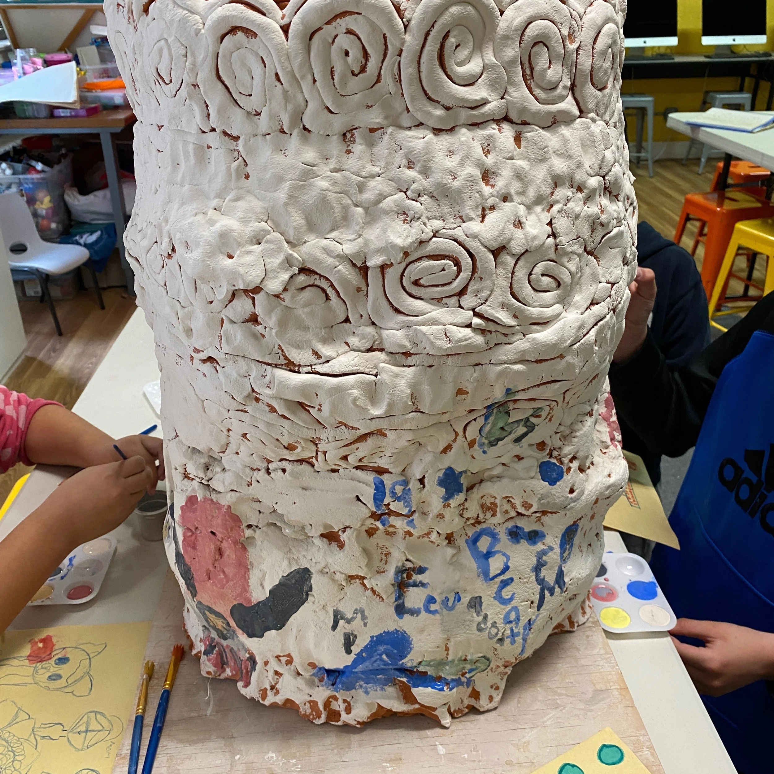 Close up of large coiled pot with white underglaze. Small hands are in the frame painting with underglazes.
