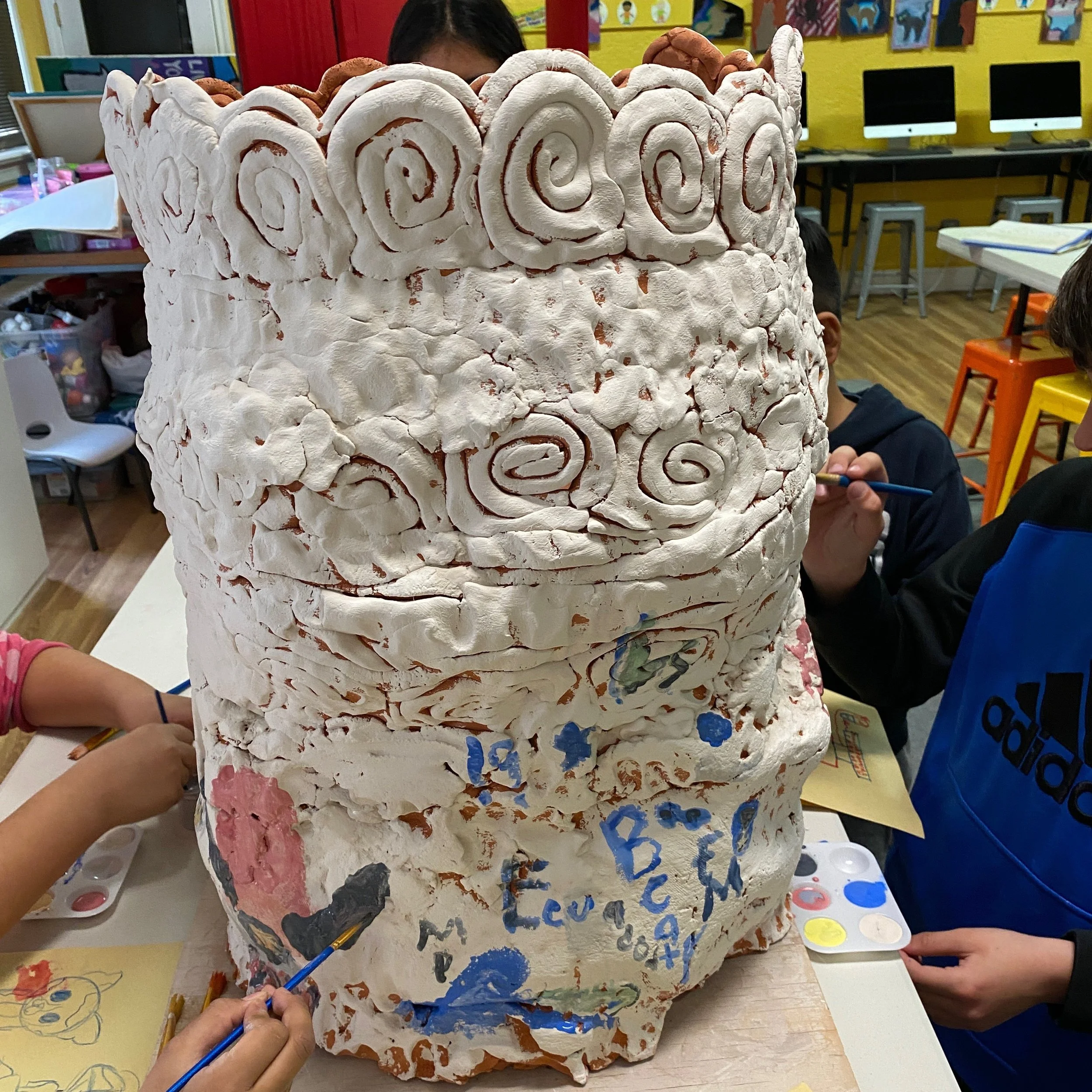 Four young students with paint palettes of underglaze paint on the pot.