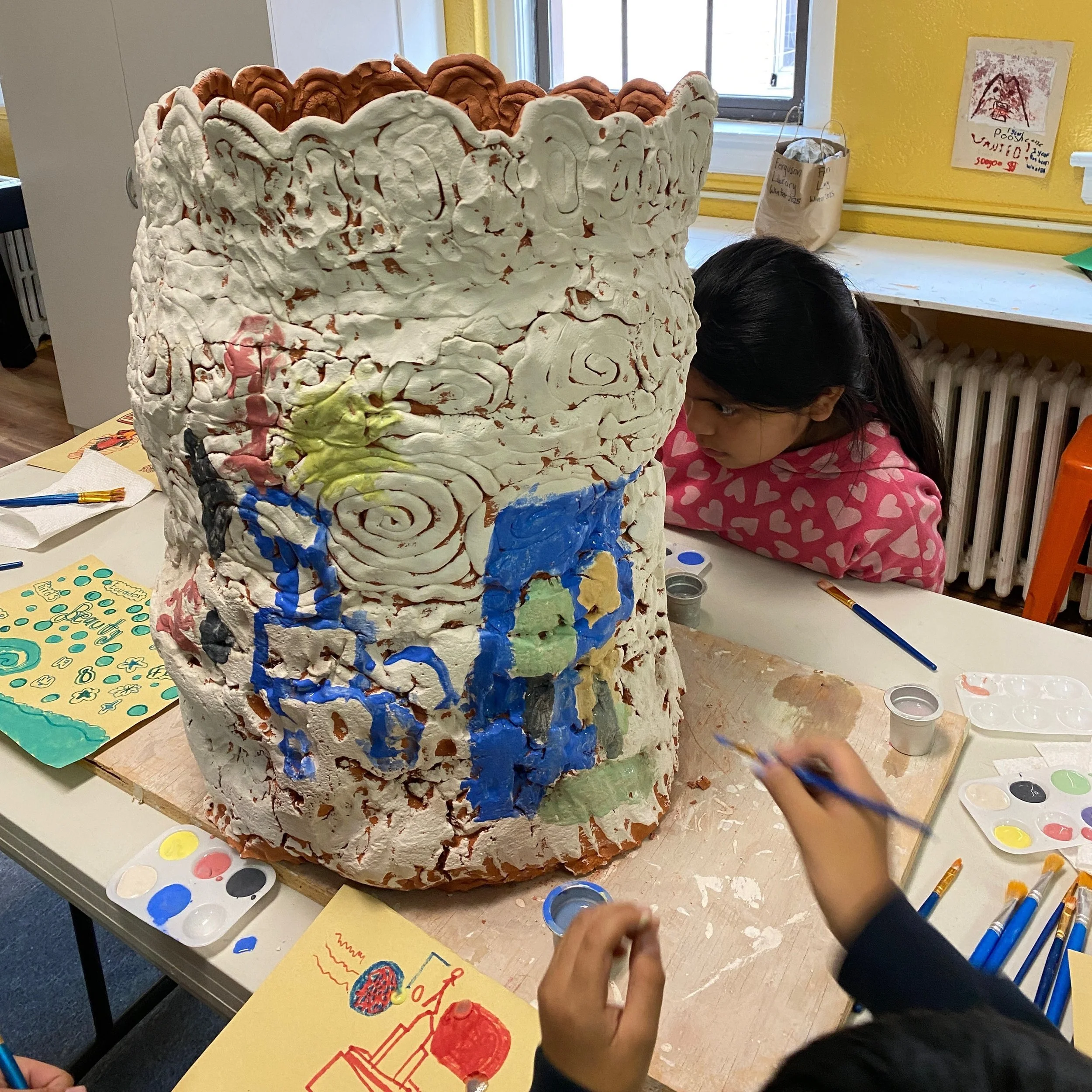 A young girl in a pink sweatshirt leans in in concentration as she paints the pot.