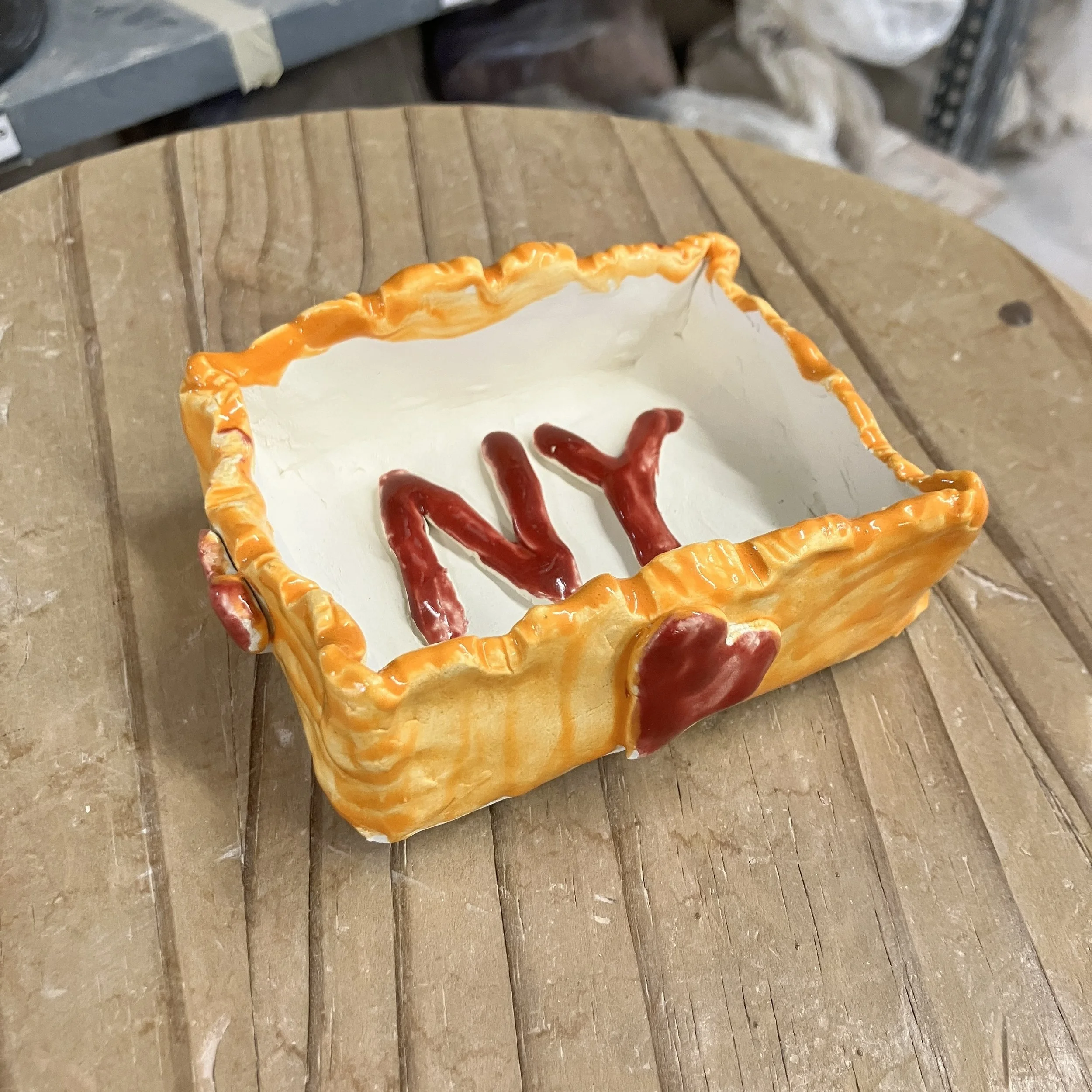 Ceramic box with an orange exterior with red hearts and a white interior and the initials NY.