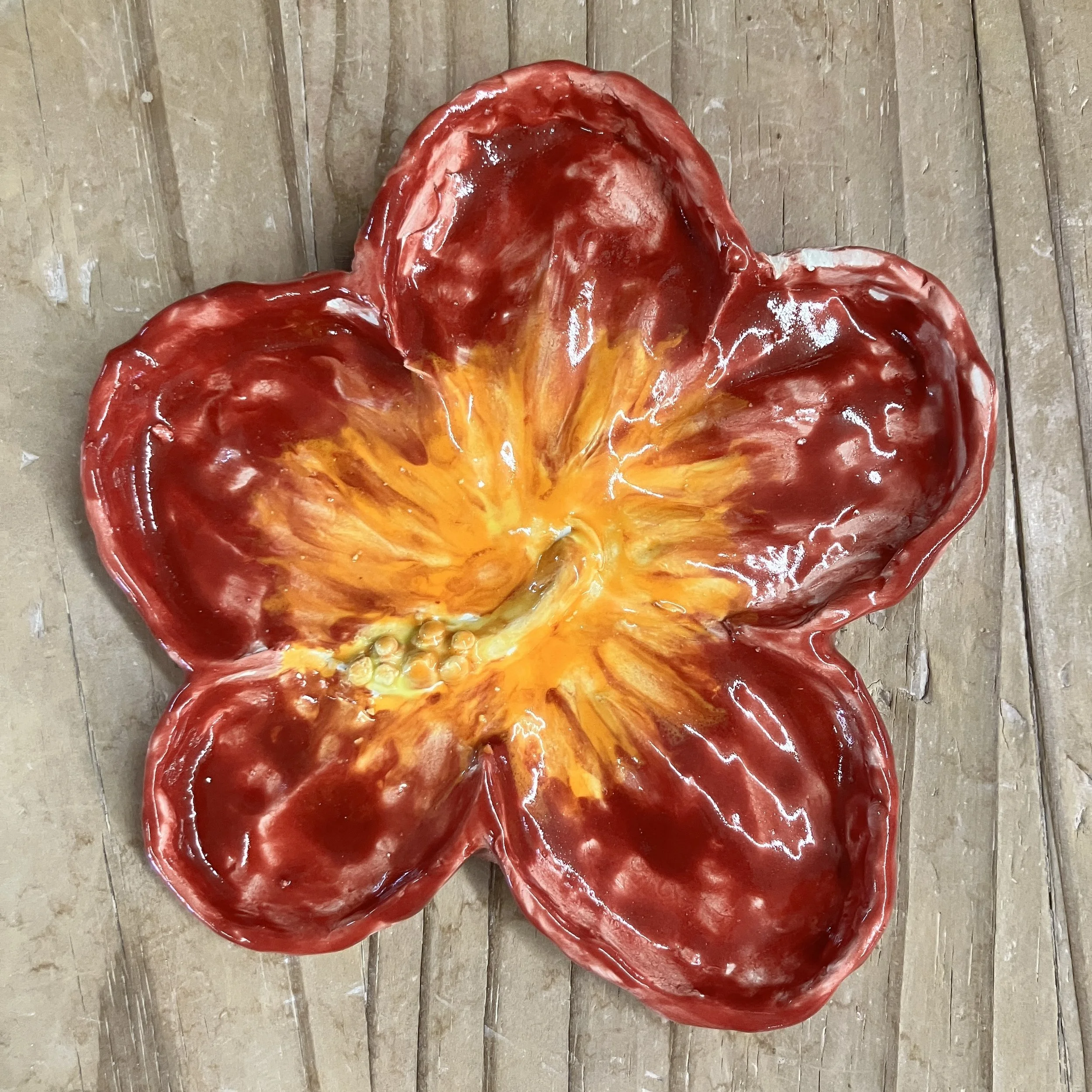 A ceramic dish shaped and painted like a red and orange hibiscus flower.