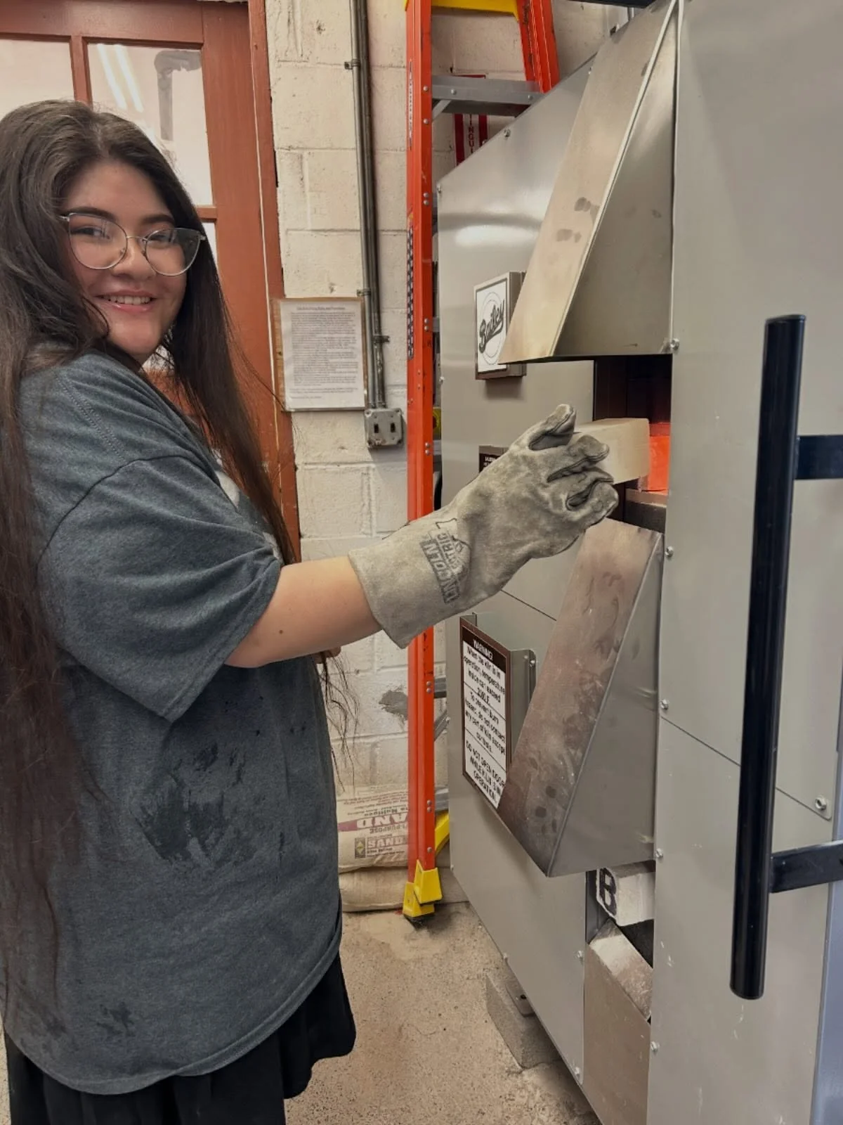Second Year Artist-in-Residence Christine Raposas checks the peephole on a gas firing in preparation for the upcoming Concurrent Artists-in-Residence exhibitions at Clay Art Center Gallery. Christine will present recent work in &ldquo;Living A Dream,