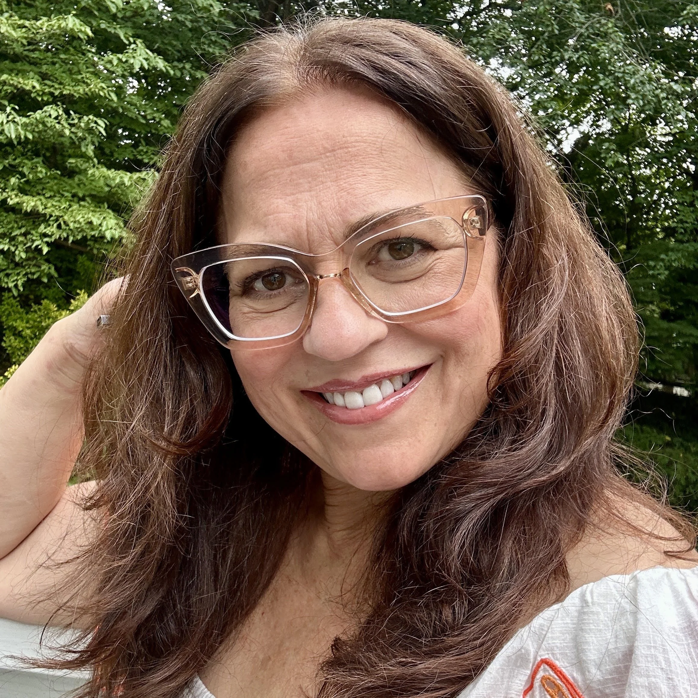 A woman with long brown hair and glasses smiles into the camera.