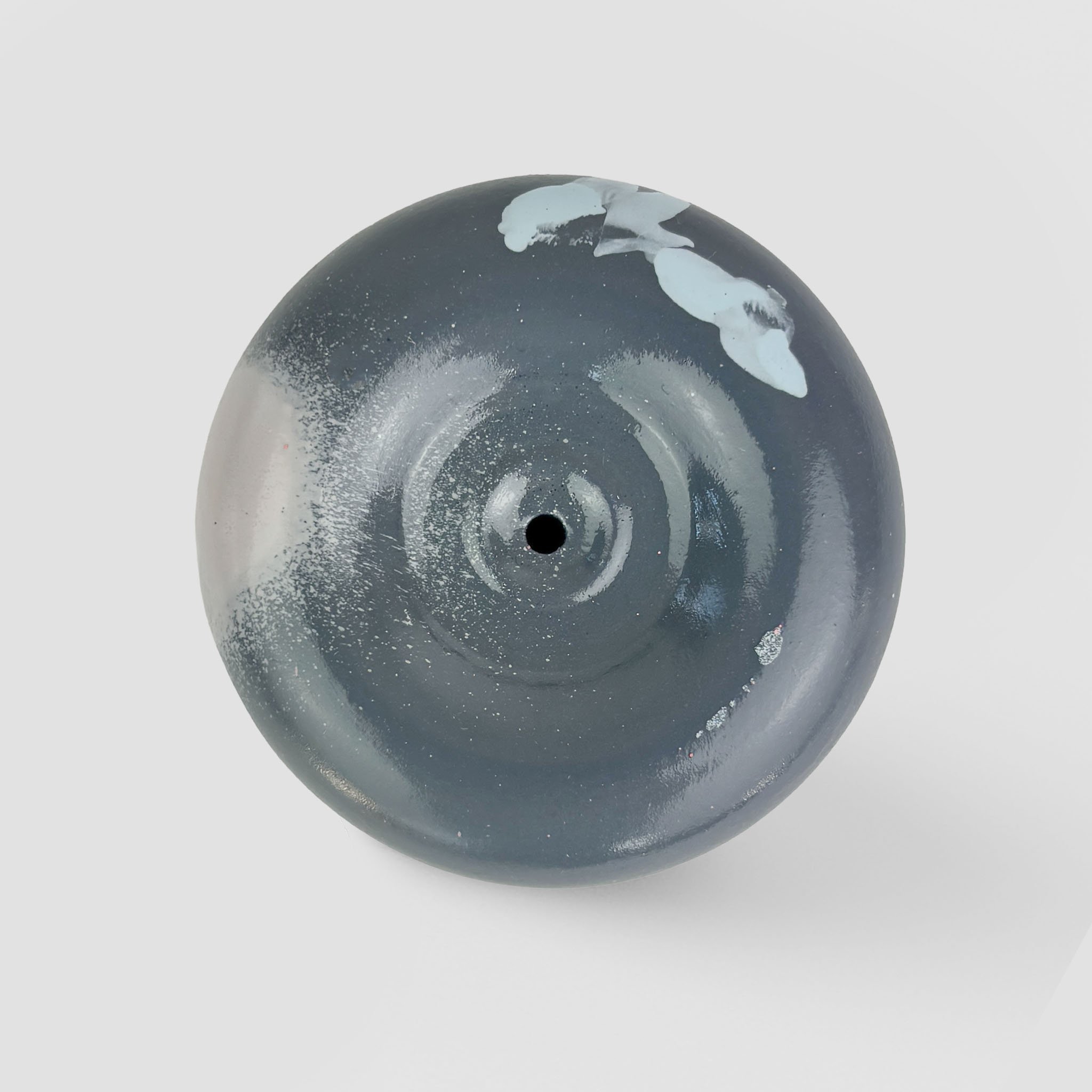 Top view of a round, black, and gray skateboard wheel with white paint splatters and a central hole.