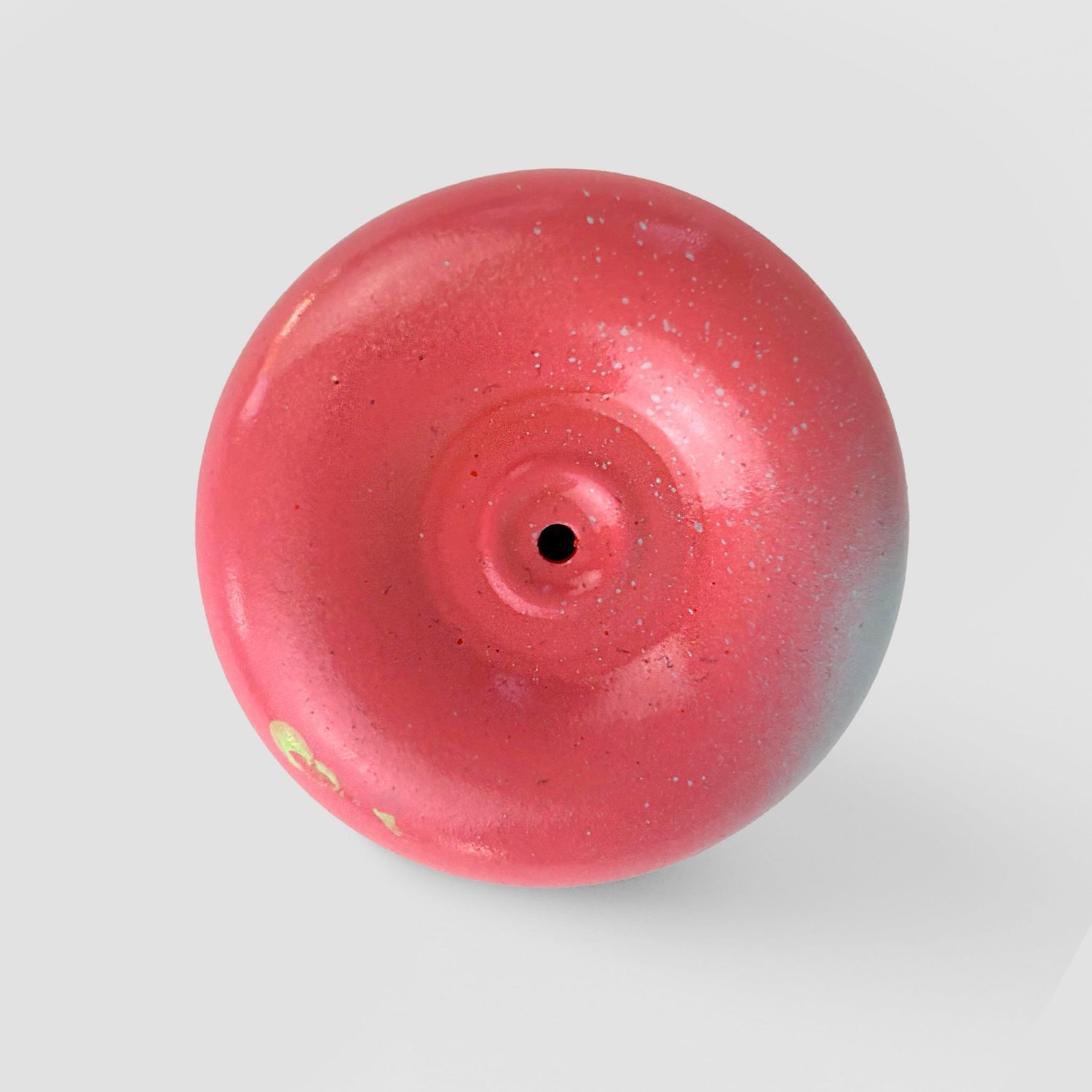 Top view of a pink ceramic fire alarm pull station with a small hole in the center on a light gray background.