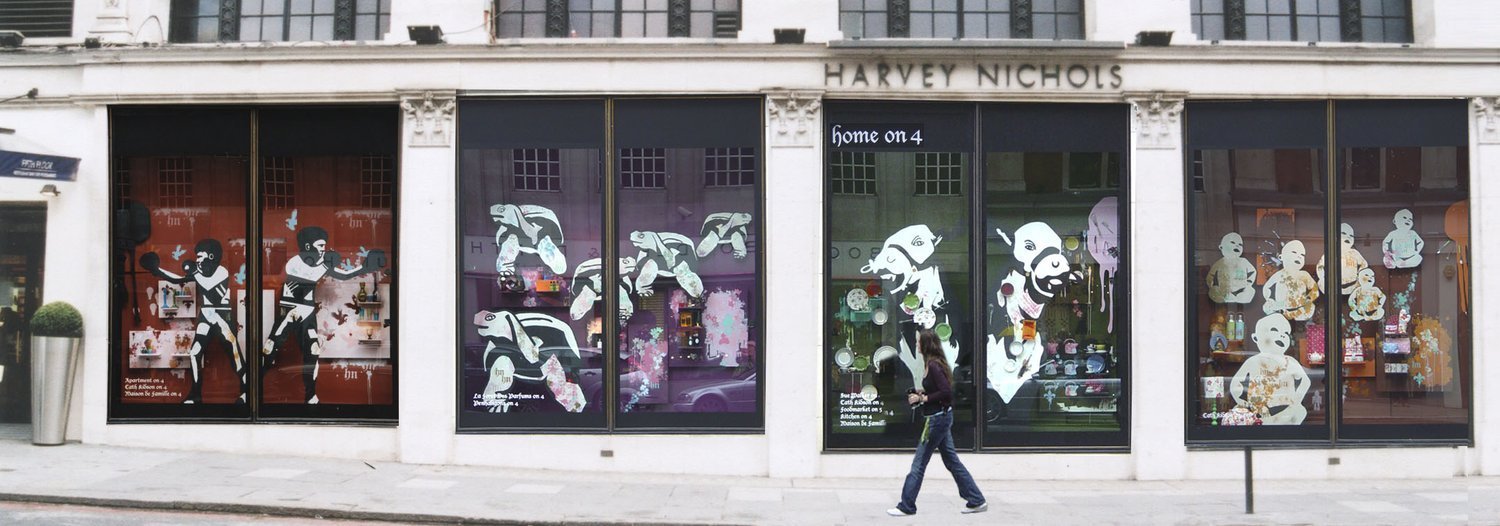 Storefront with large windows decorated with illustrated figures of women, animals, and objects, and the sign "Harvey Nichols" above the windows. A woman walks past the storefront.