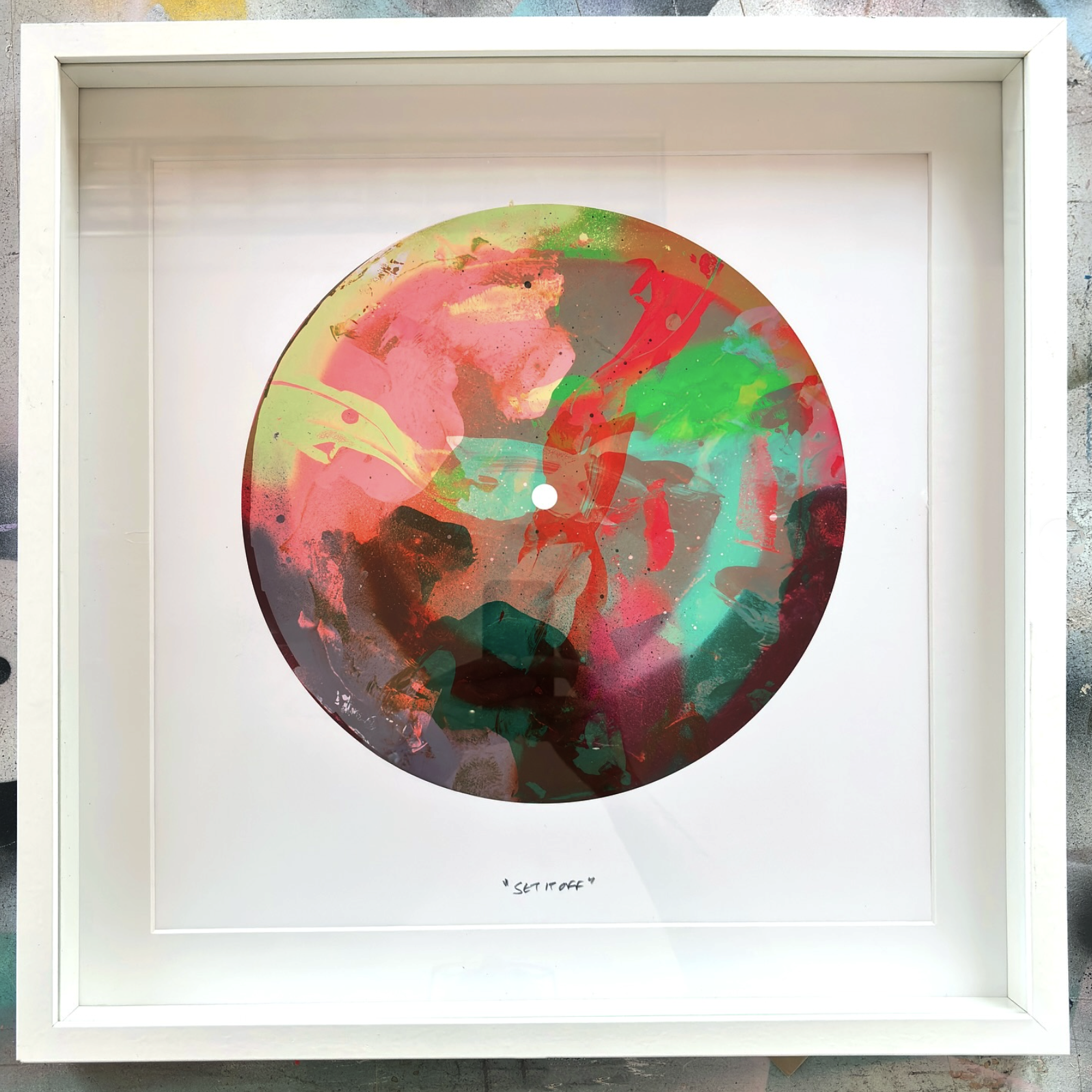 Colorful abstract round artwork with splashes of red, green, teal, and black, framed in a white frame.