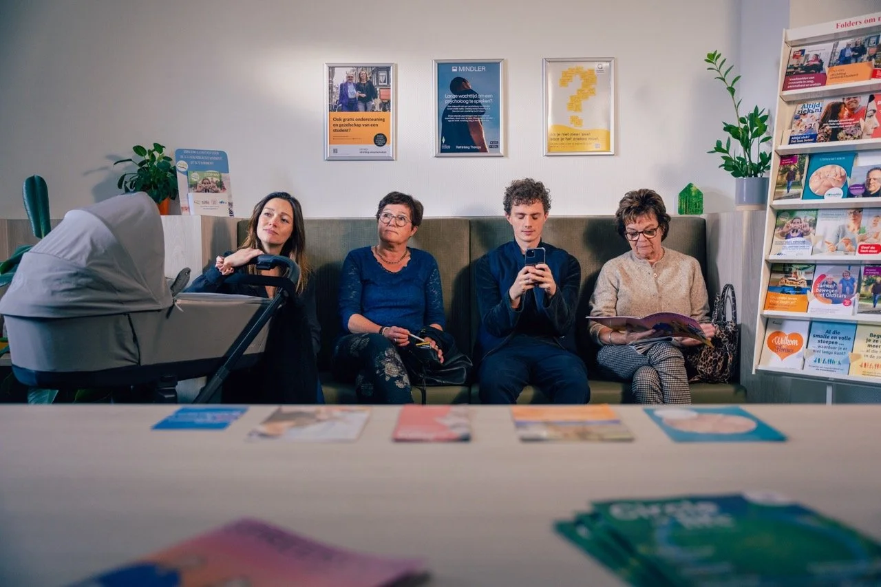 Vier patiënten zitten op een rij te wachten in een wachtkamer.