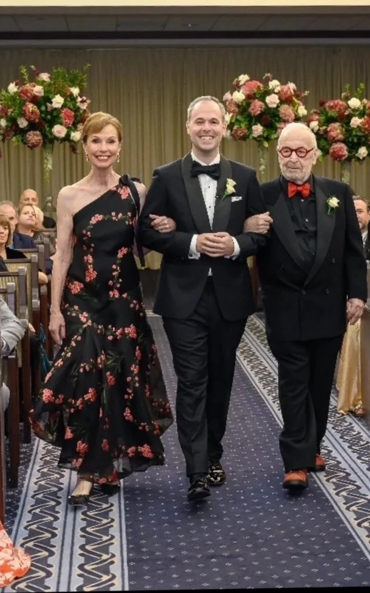 Lucy Reitzfeld and husband Robert at their son’s wedding - silk cloqué one shoulder dress