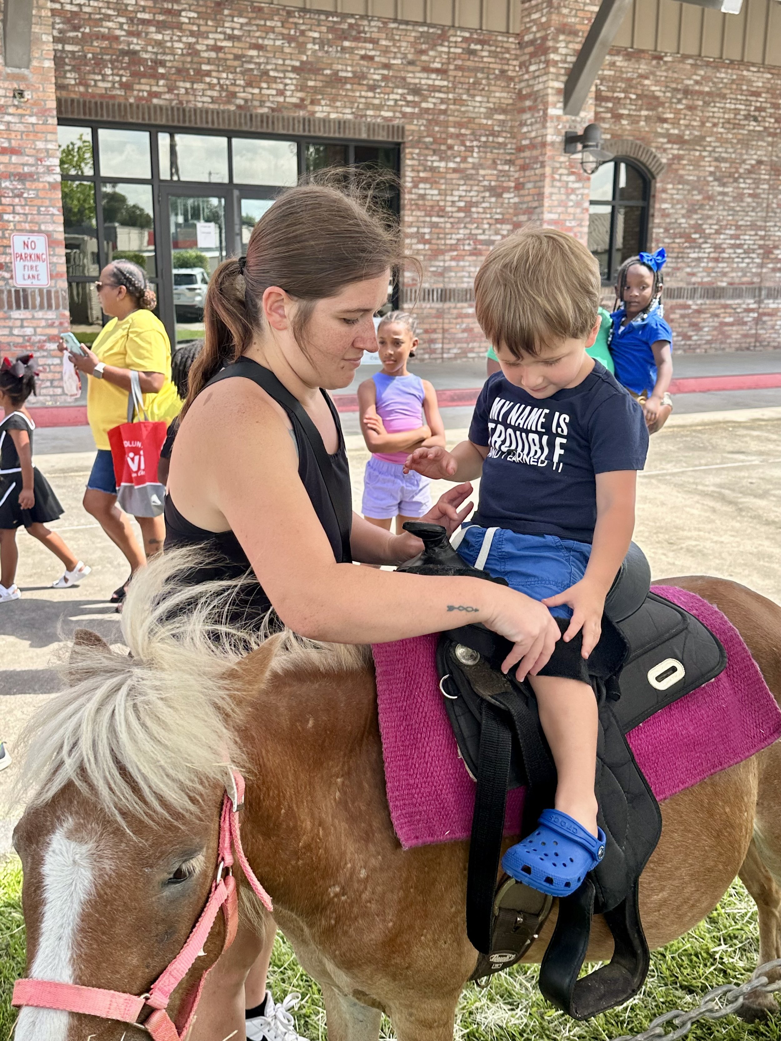  Laken Naquin helps to buckle 3-year-old Hudson Breaux for a pony ride at the Early Childhood Day in Assumption Parish. 