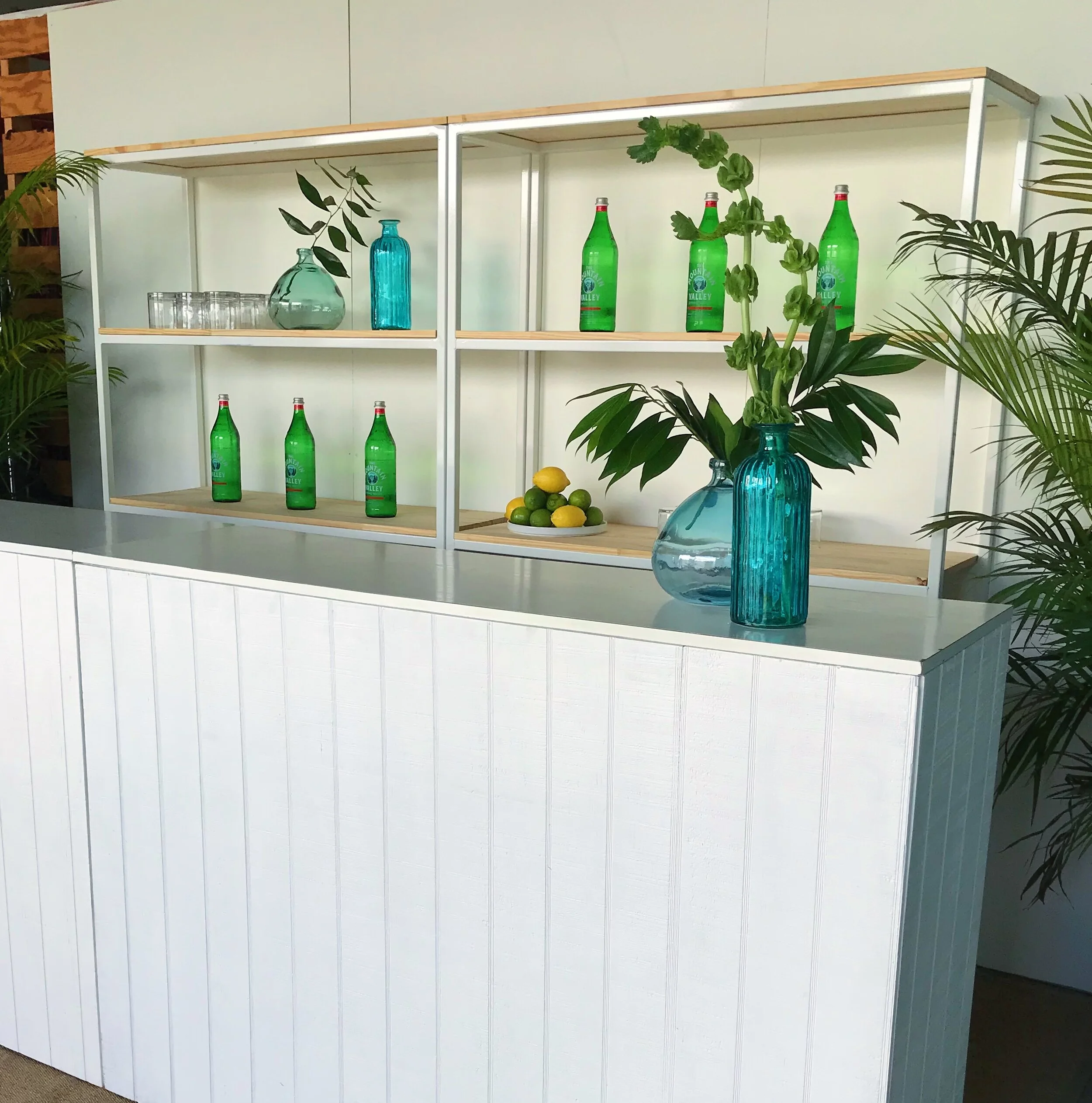White paneled bars with a shelving unit used as a back bars with bottles and plants or an event in Miami