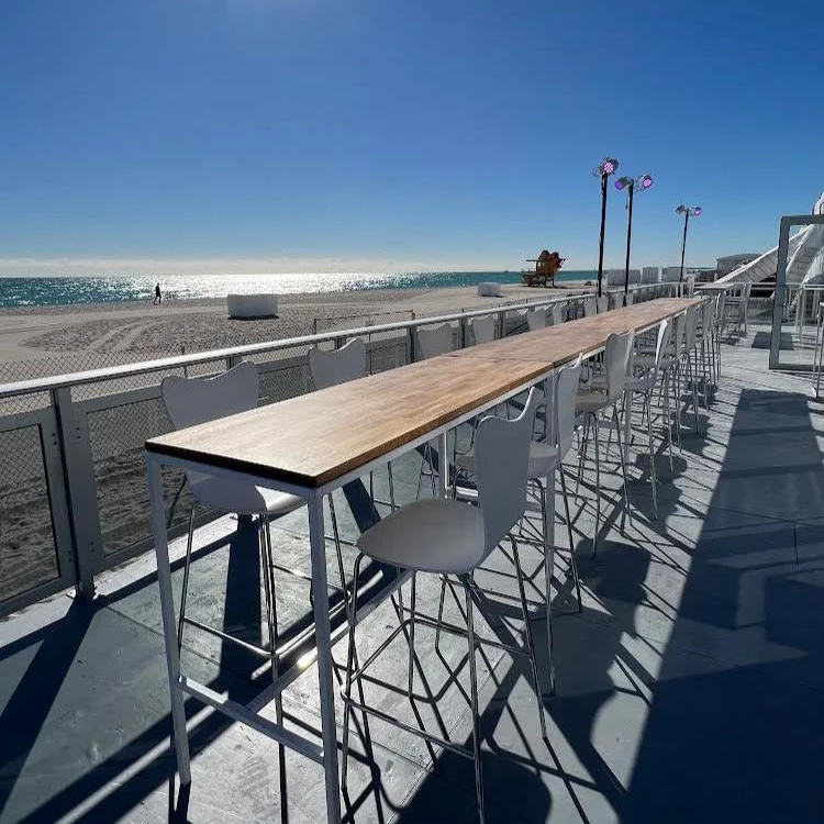 Bar Height tables with oak tops connected together to form a long line of tables facing the ocean on Miami Beach