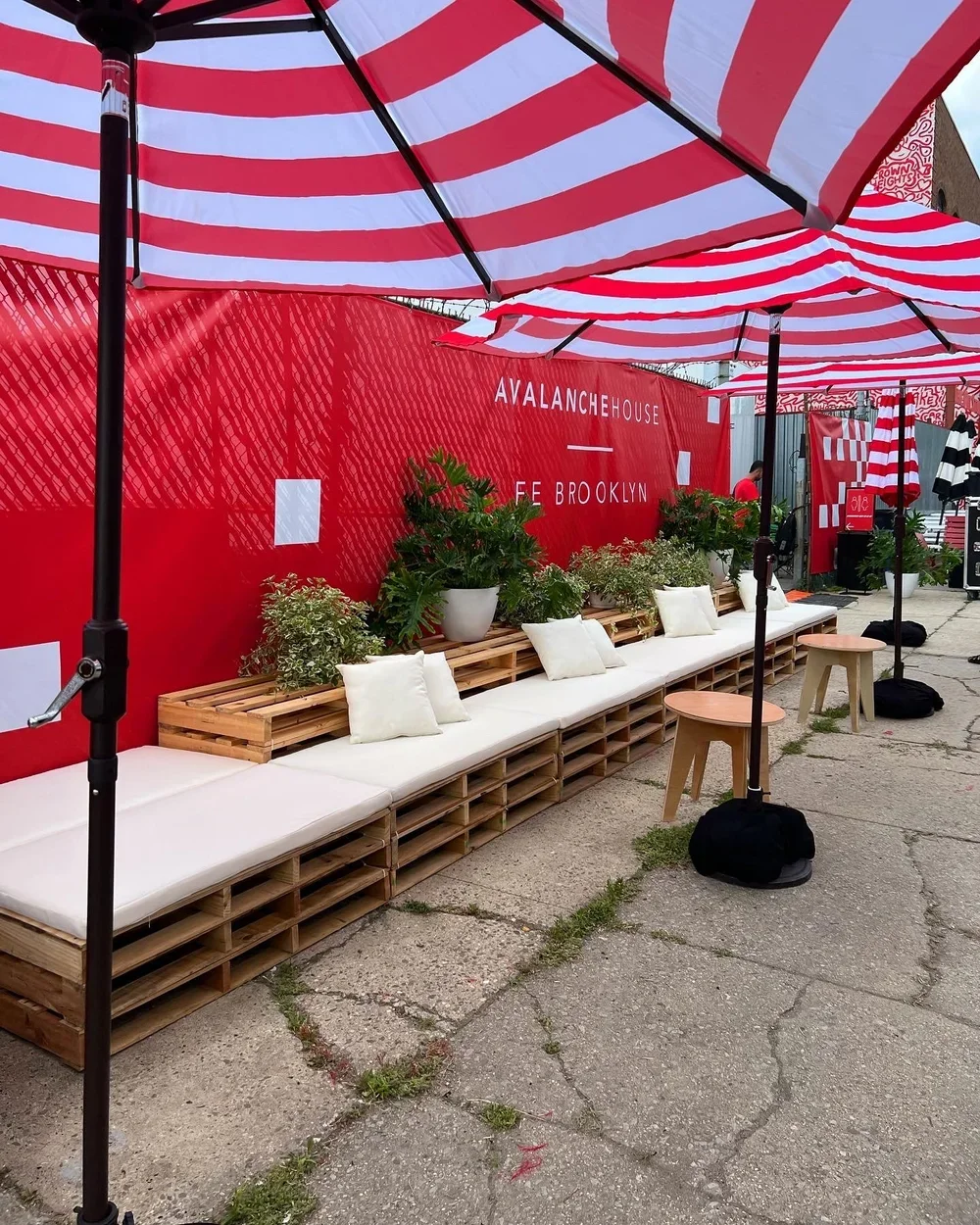 A linear seating arrangement made out of wood pallets with cushions and striped umbrellas