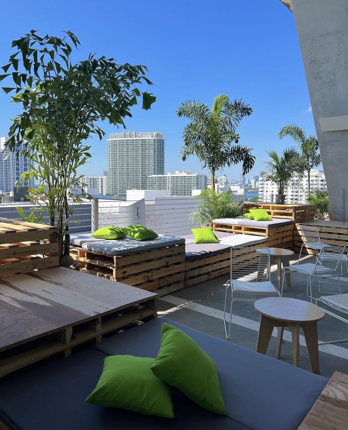 Pallet seating with gray cushions and green pillows and plants in between them and the Miami Beach skyline