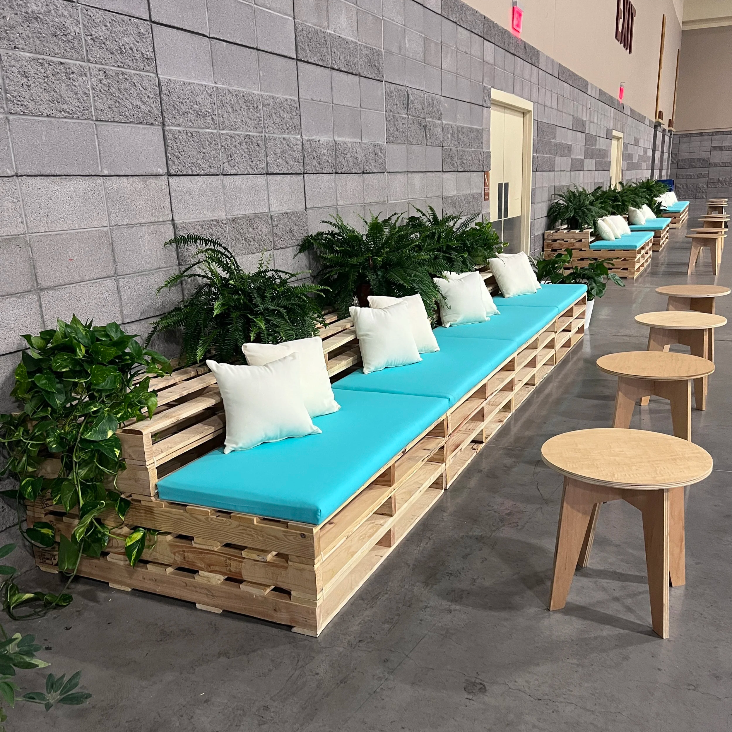 Event furniture made out of wood pallets set along a conference wall with Aqua cushions and plants