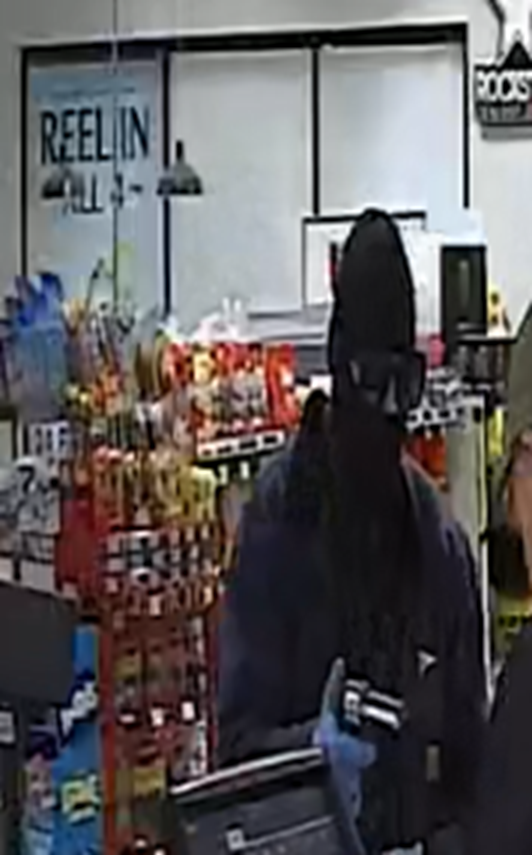 Picture of a robbery suspect wearing a black mask, sunglasses, and dark clothing while armed with a gun.
