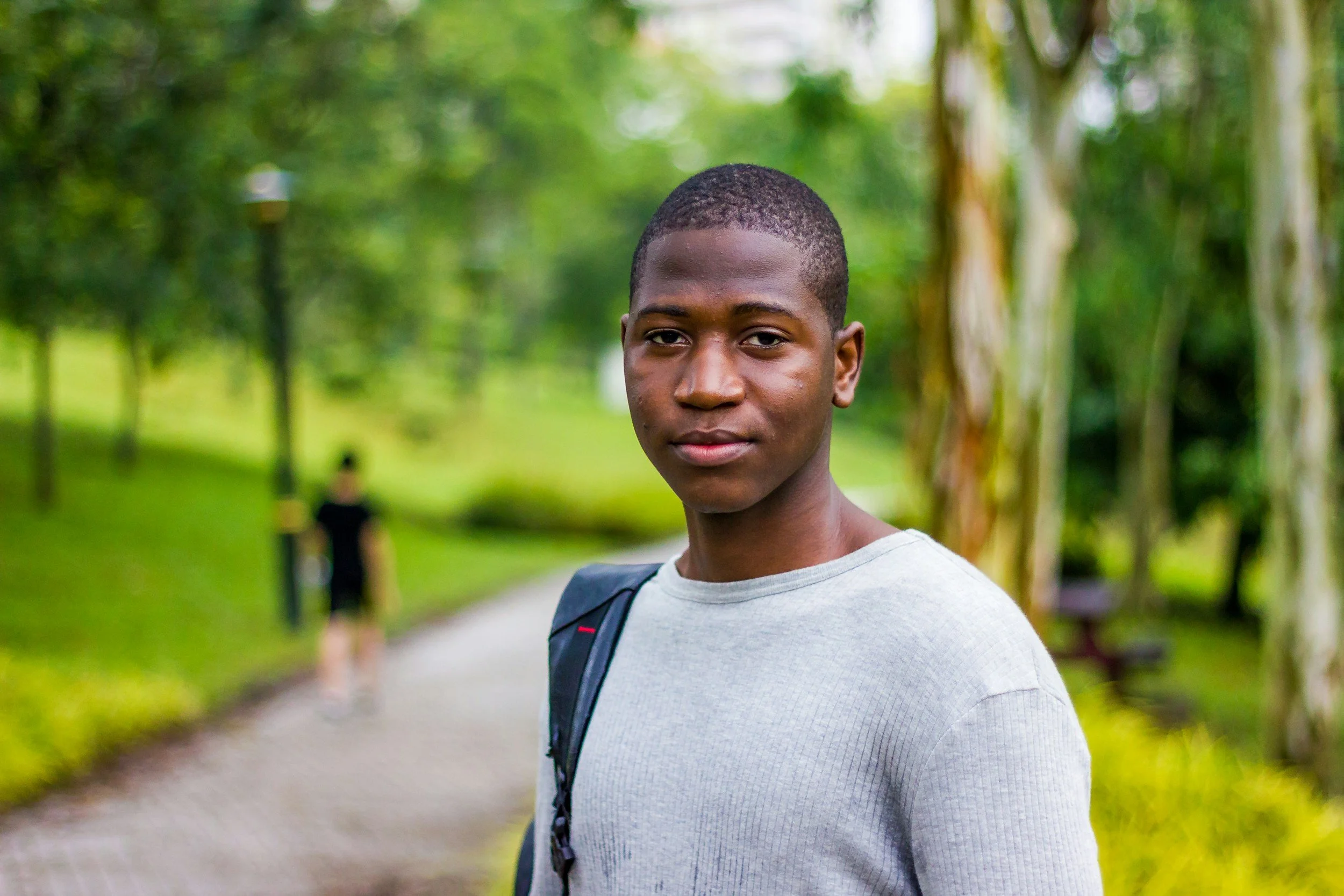 A man in a park looks at the camera. He is wearing a grey jumper.