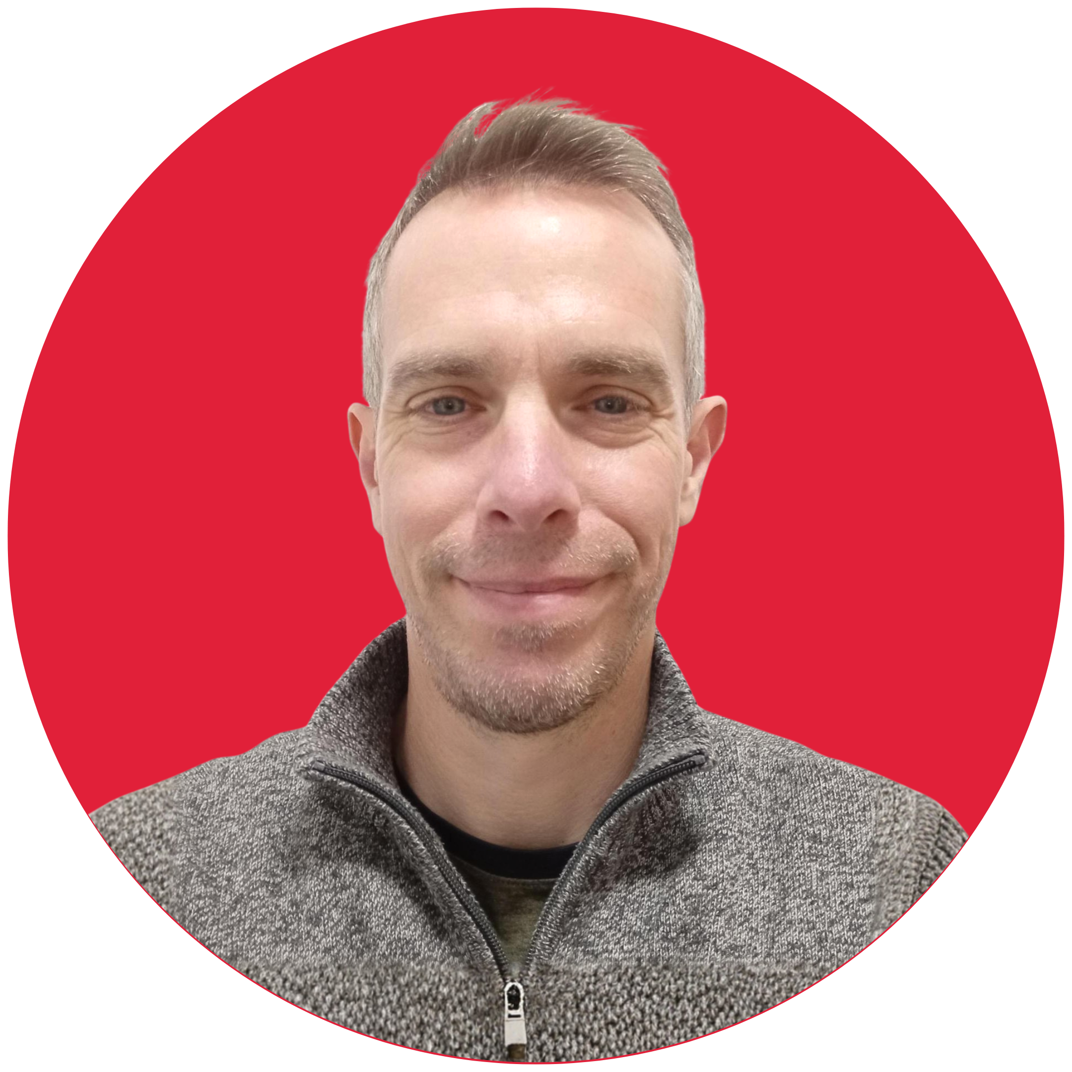 A grey-haired man smiles at the camera. He is wearing a grey fleece and is set against a red background.